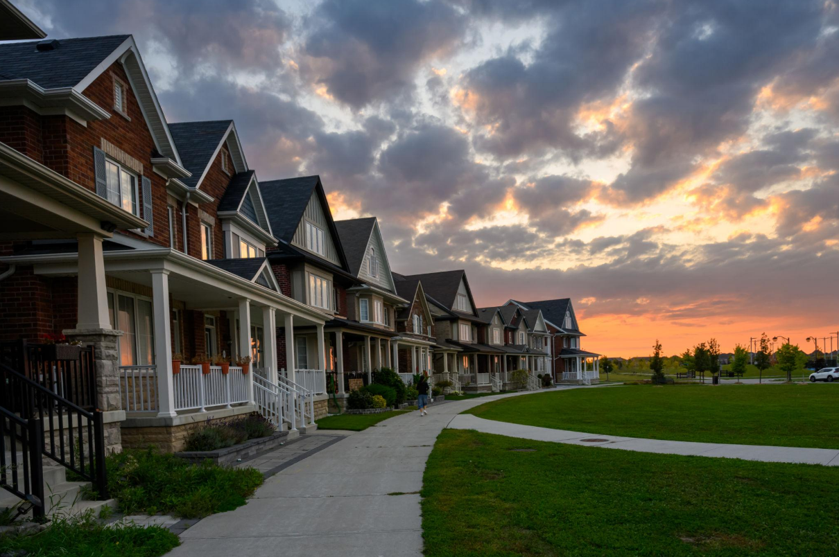 Houses with porches along a curved pathway during sunset with a grassy lawn and cloudy sky in the background.