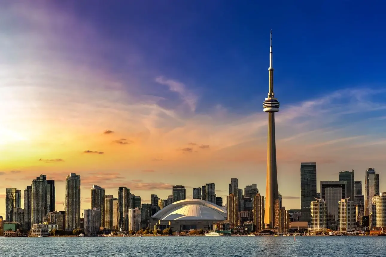 Sunset view of Toronto skyline with CN Tower, Rogers Centre stadium, and high-rise buildings across the water.