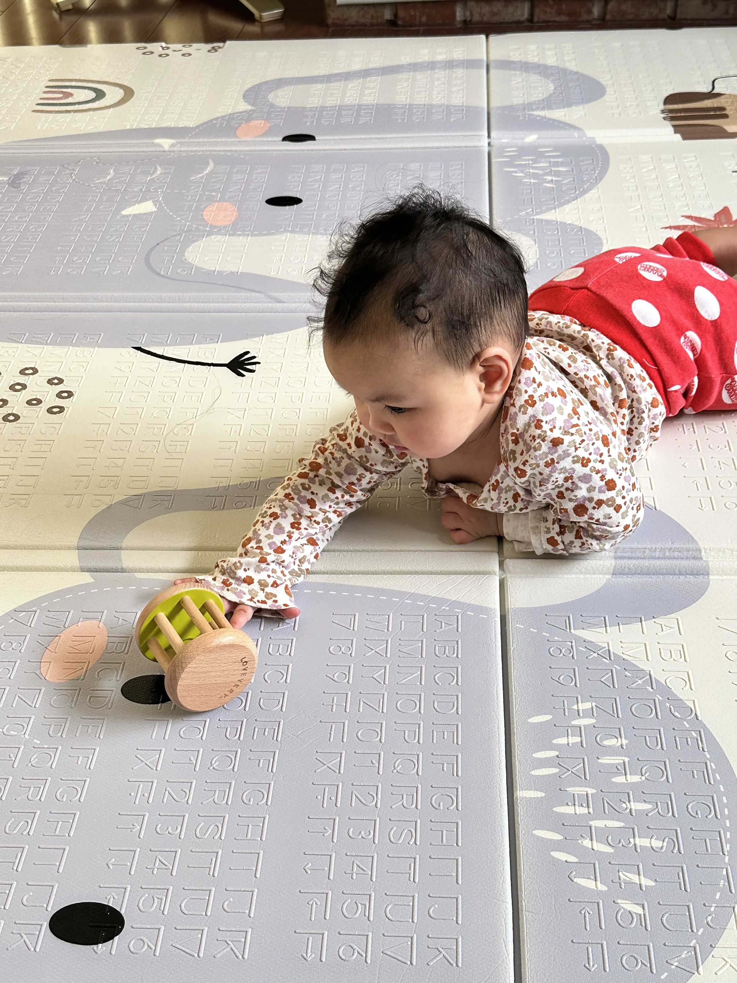 A baby girl lying on her stomach on an interactive mat, reaching out to touch a toy.