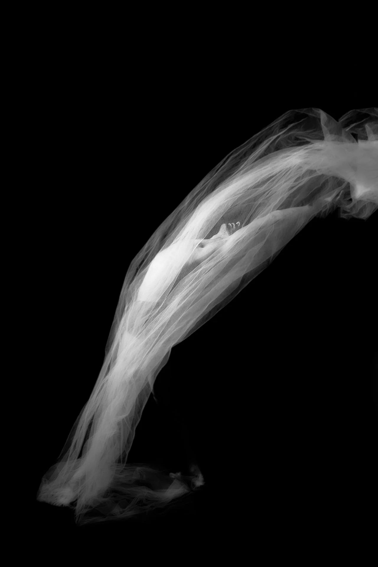 Uma imagem em preto e branco de uma mulher com um véu fluindo ao seu redor, criando uma cena artística e etérea.