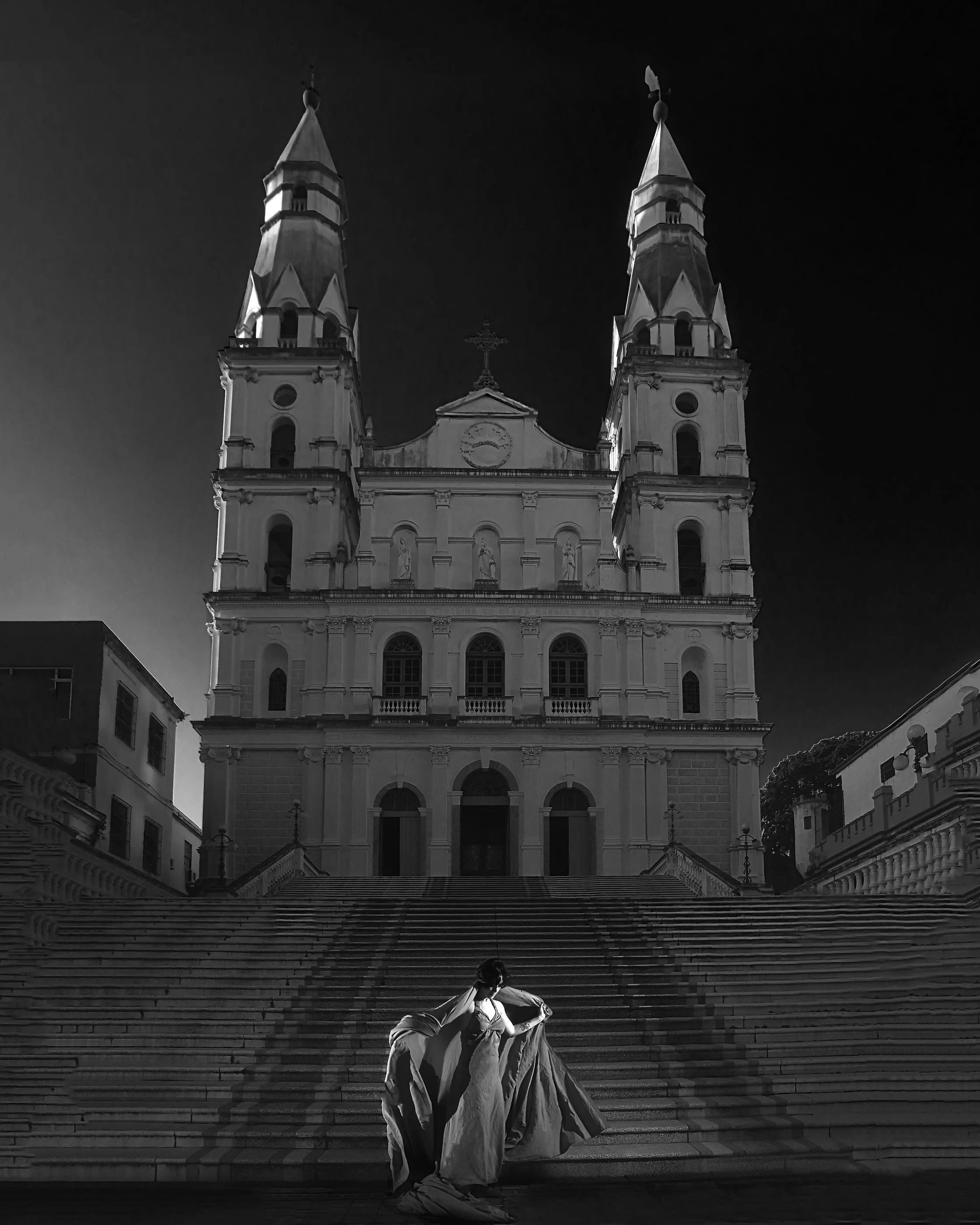 Mulher com vestido longo descendo as escadas em frente a uma catedral.