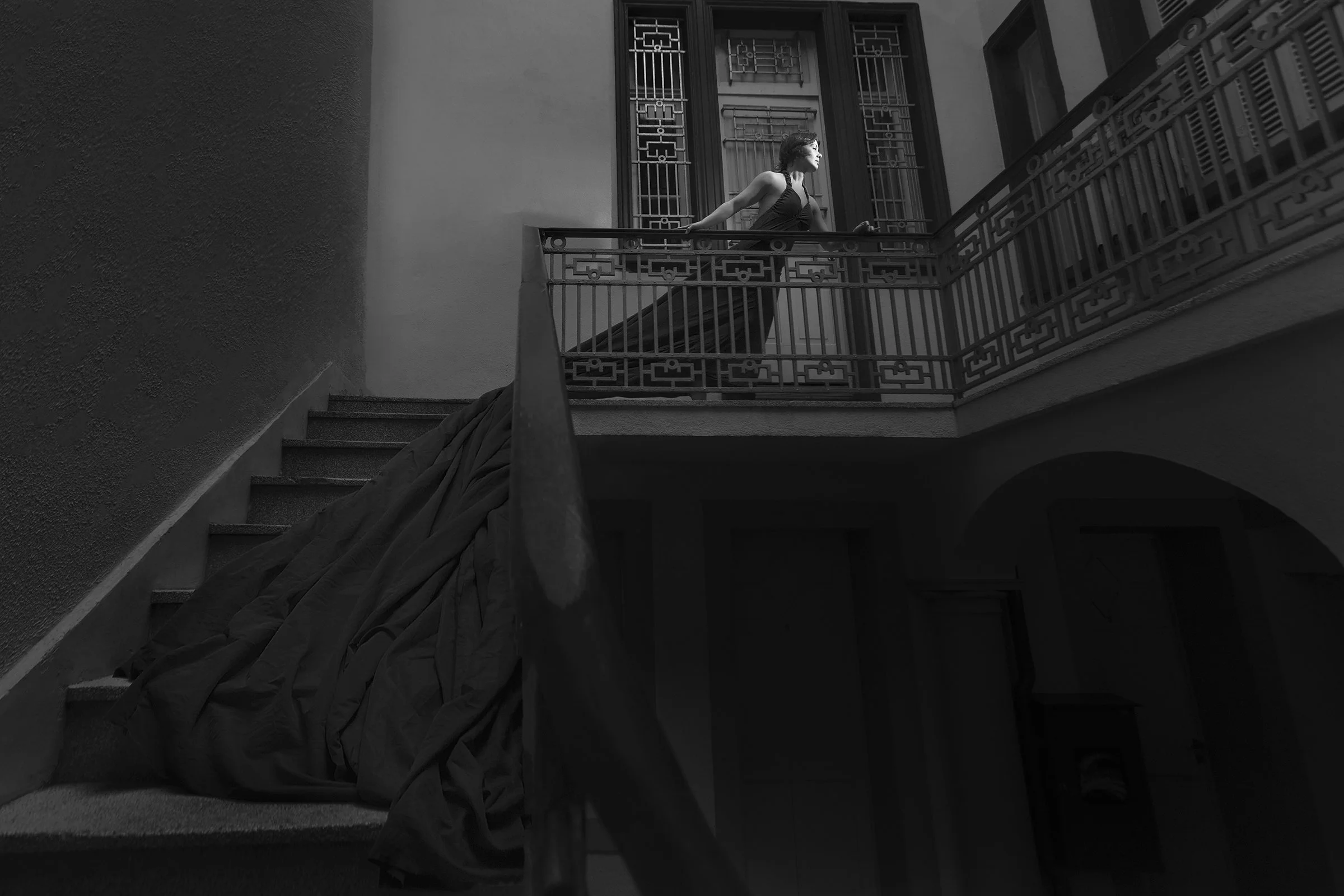 Mulher de vestido longo de pé na sacada de um interior com escada ao lado