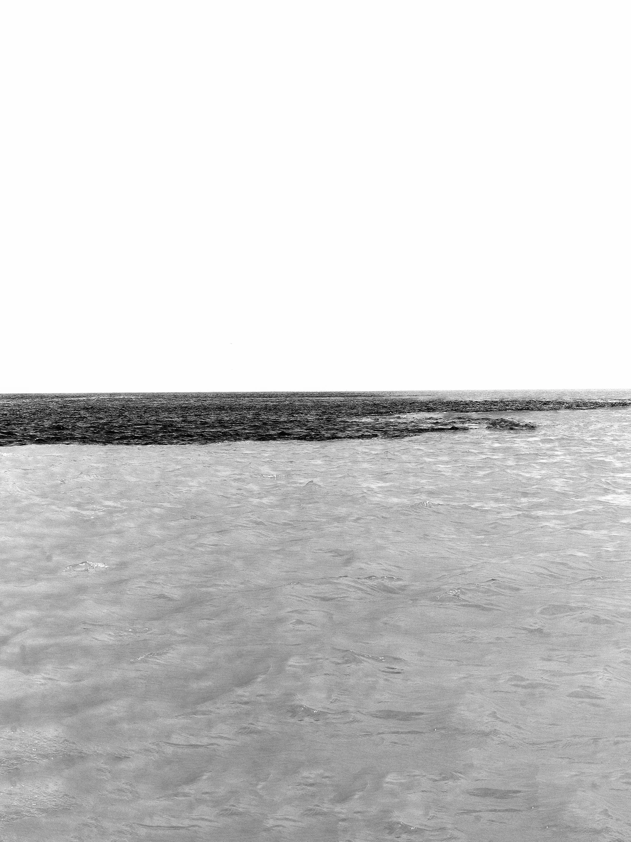 Imagem em preto e branco de um mar ou oceano com horizonte visível, ondas suaves na superfície da água.