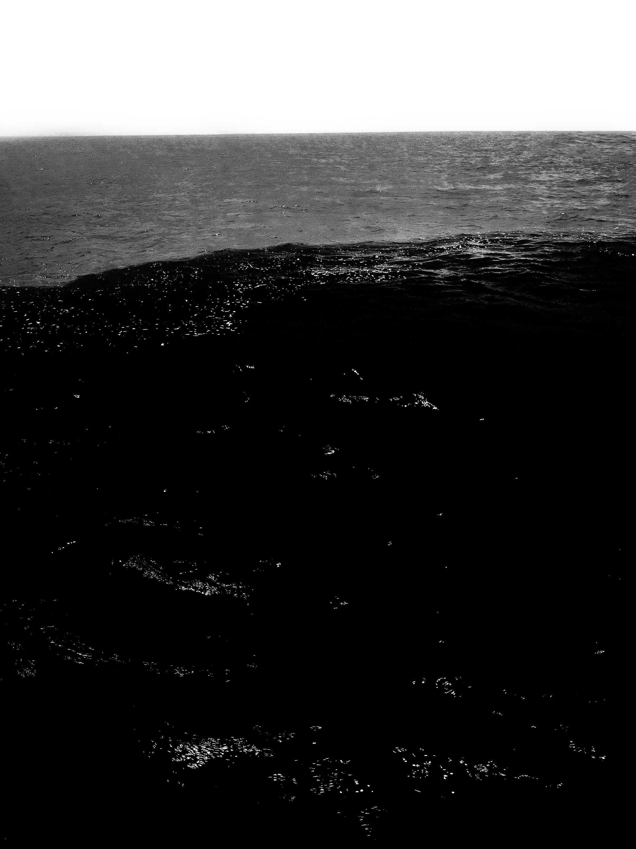 Mar aberto em preto e branco, com ondas no mar e céu claro ao fundo.