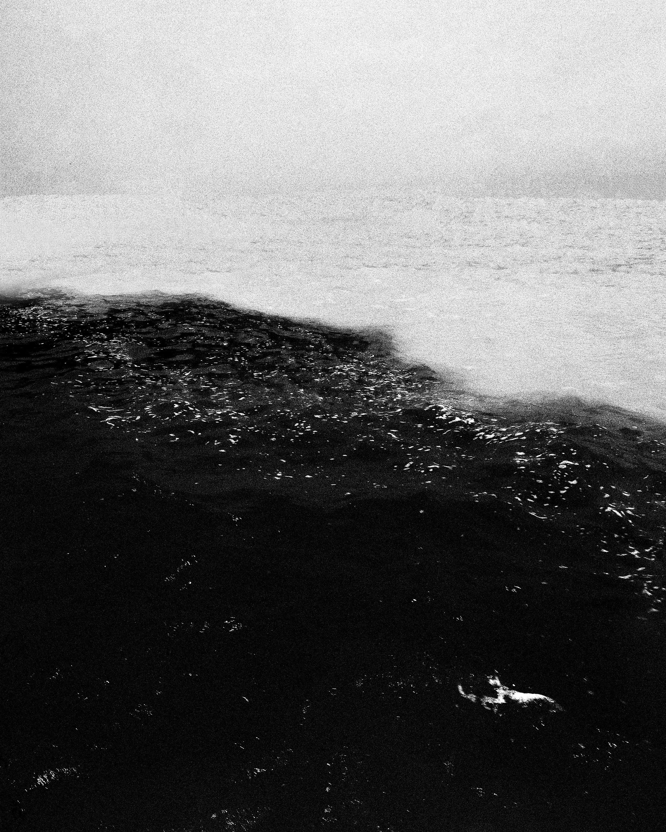 Foto em preto e branco de ondas do mar, com uma parte mais escura na parte inferior e a água clara na parte superior