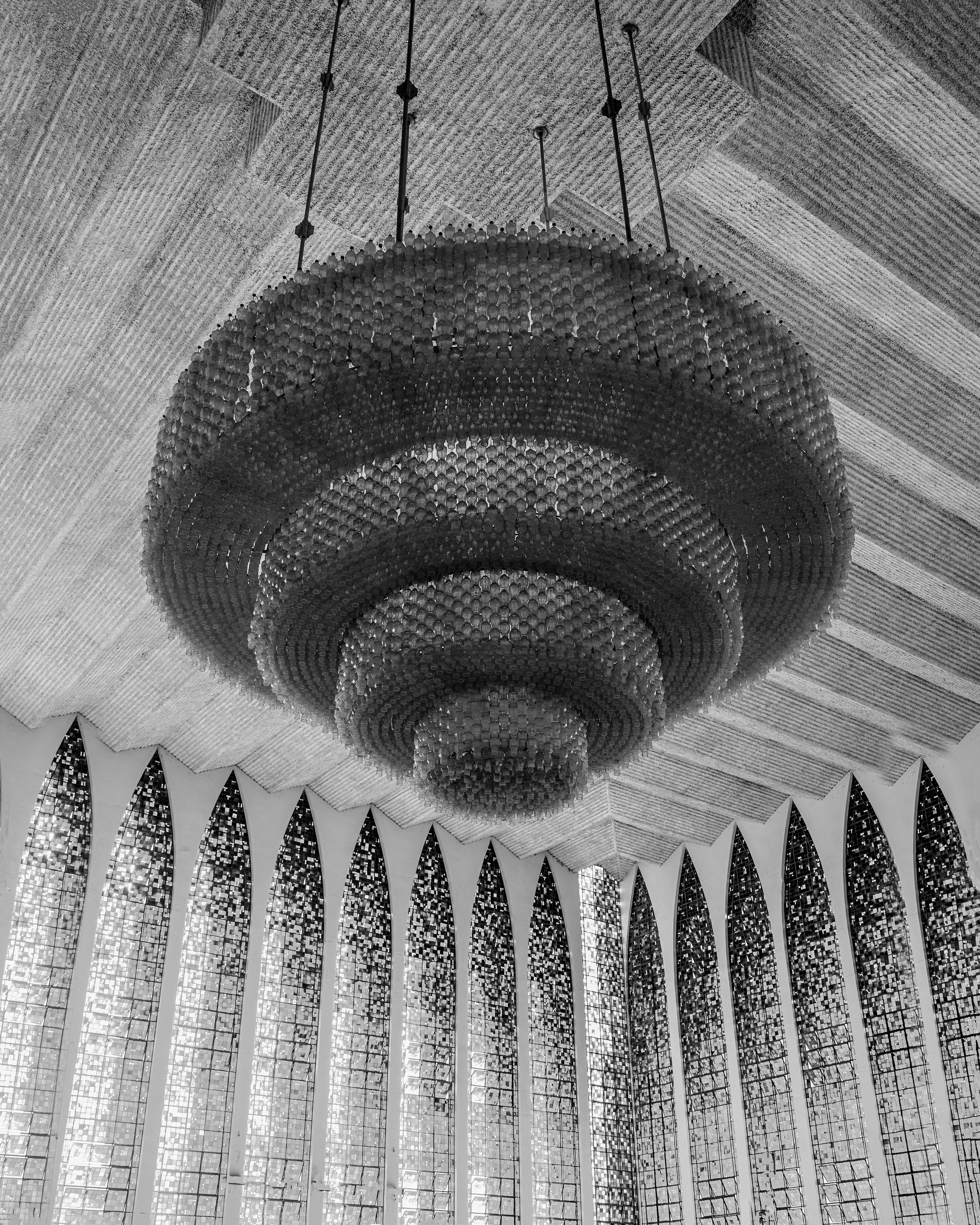 Candelabro grande pendurado de teto em uma sala com janelas altas arqueadas.
