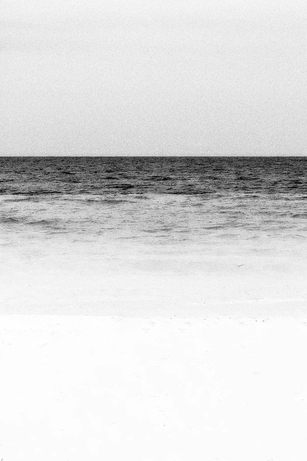 Imagem em preto e branco de uma praia, com o mar ao fundo e a areia na frente