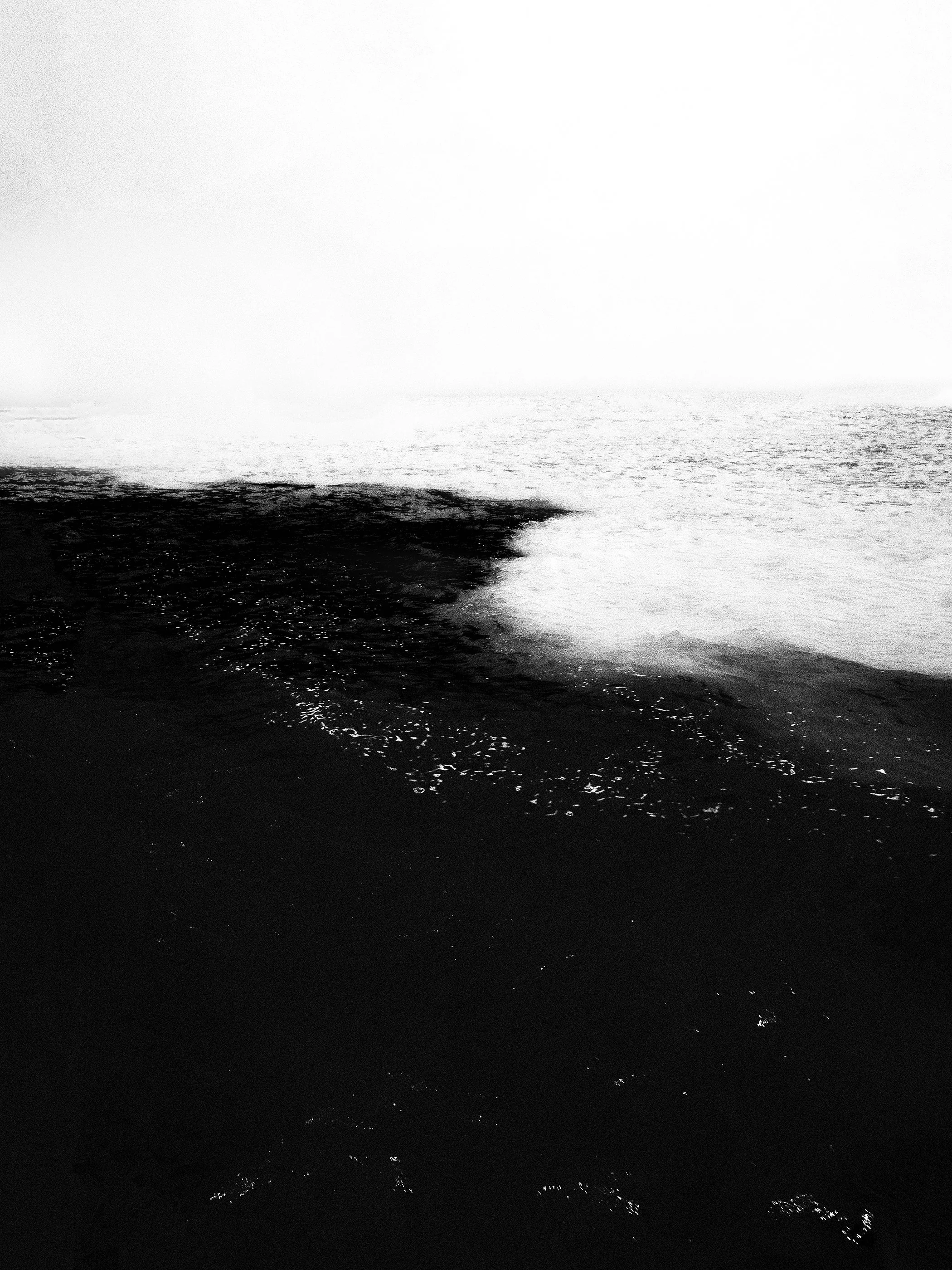 Mar profundo em maré baixa, vista de uma praia escura ao pôr do sol ou amanhecer com luz forte ao fundo.