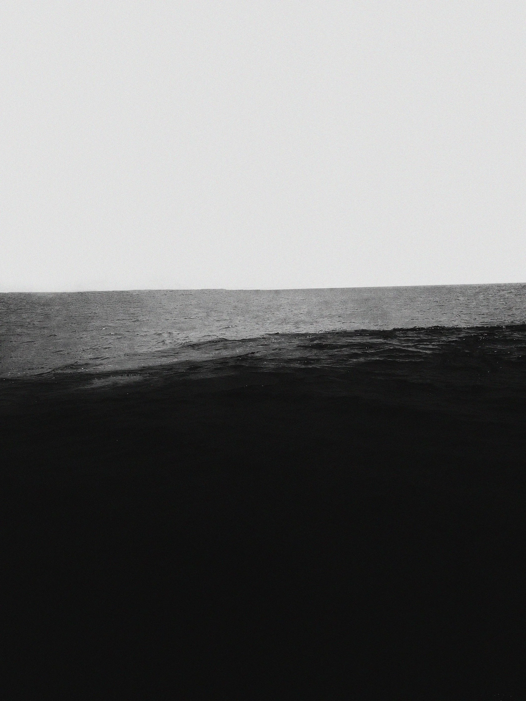 Imagem em preto e branco de uma superfície de água, possivelmente o mar, com o horizonte ao fundo sob um céu nublado.