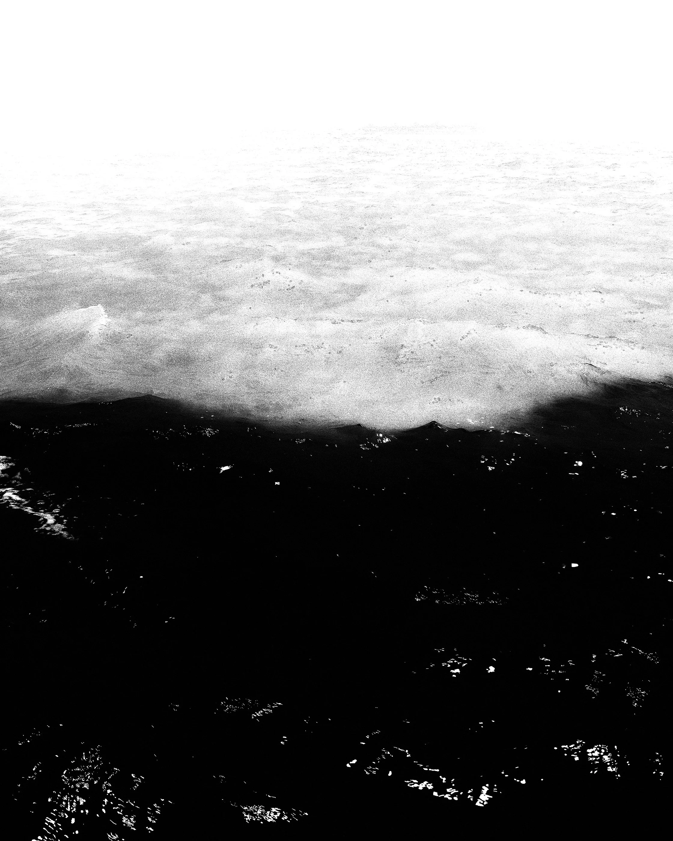 Água do mar com ondas chegando na praia em preto e branco.