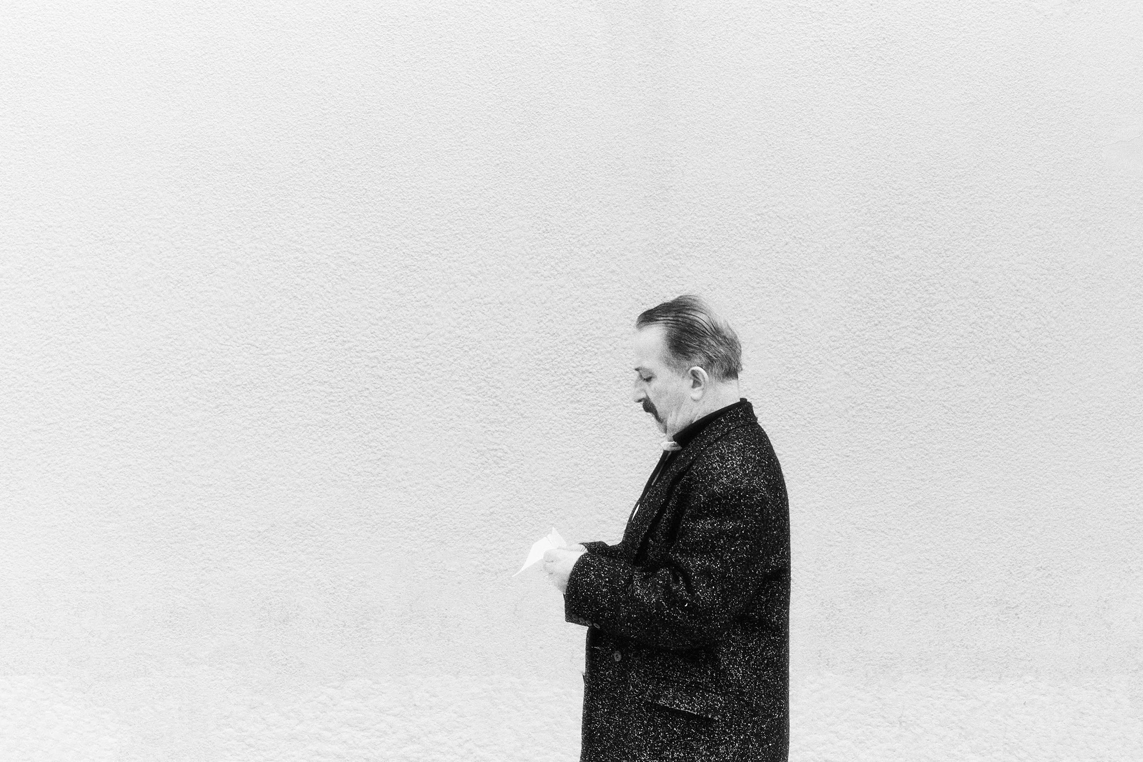 Homem vestido com sobretudo pontilhado lendo uma folha de papel contra uma parede branca