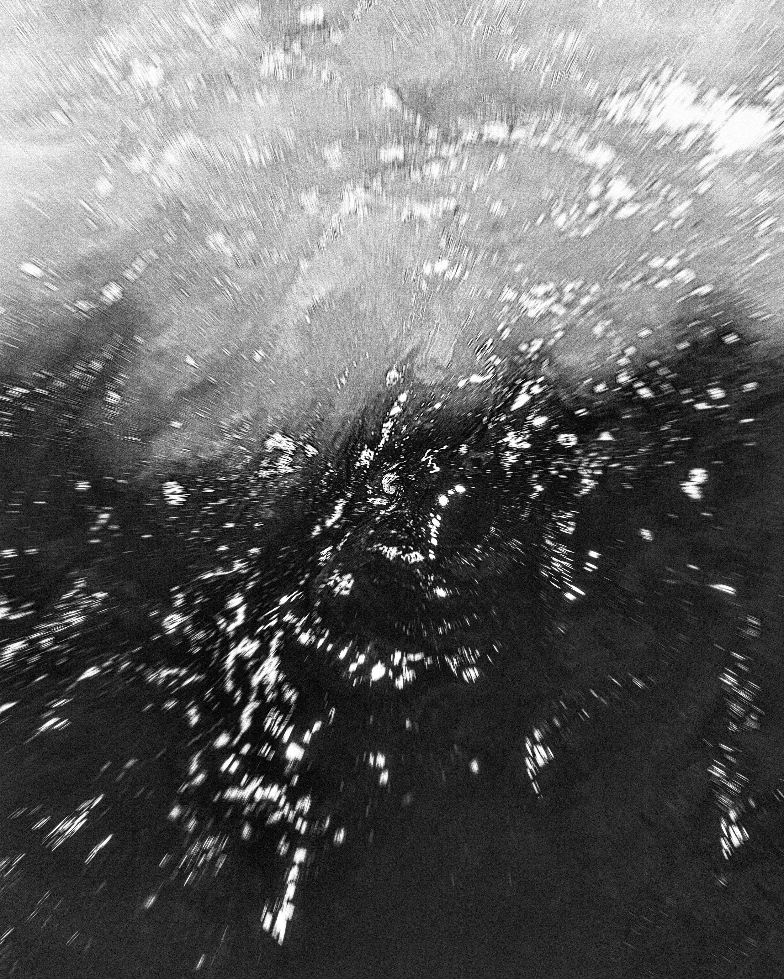 Imagem de uma galáxia com movimento, em tons de preto e branco, com estrelas e um centro brilhante.