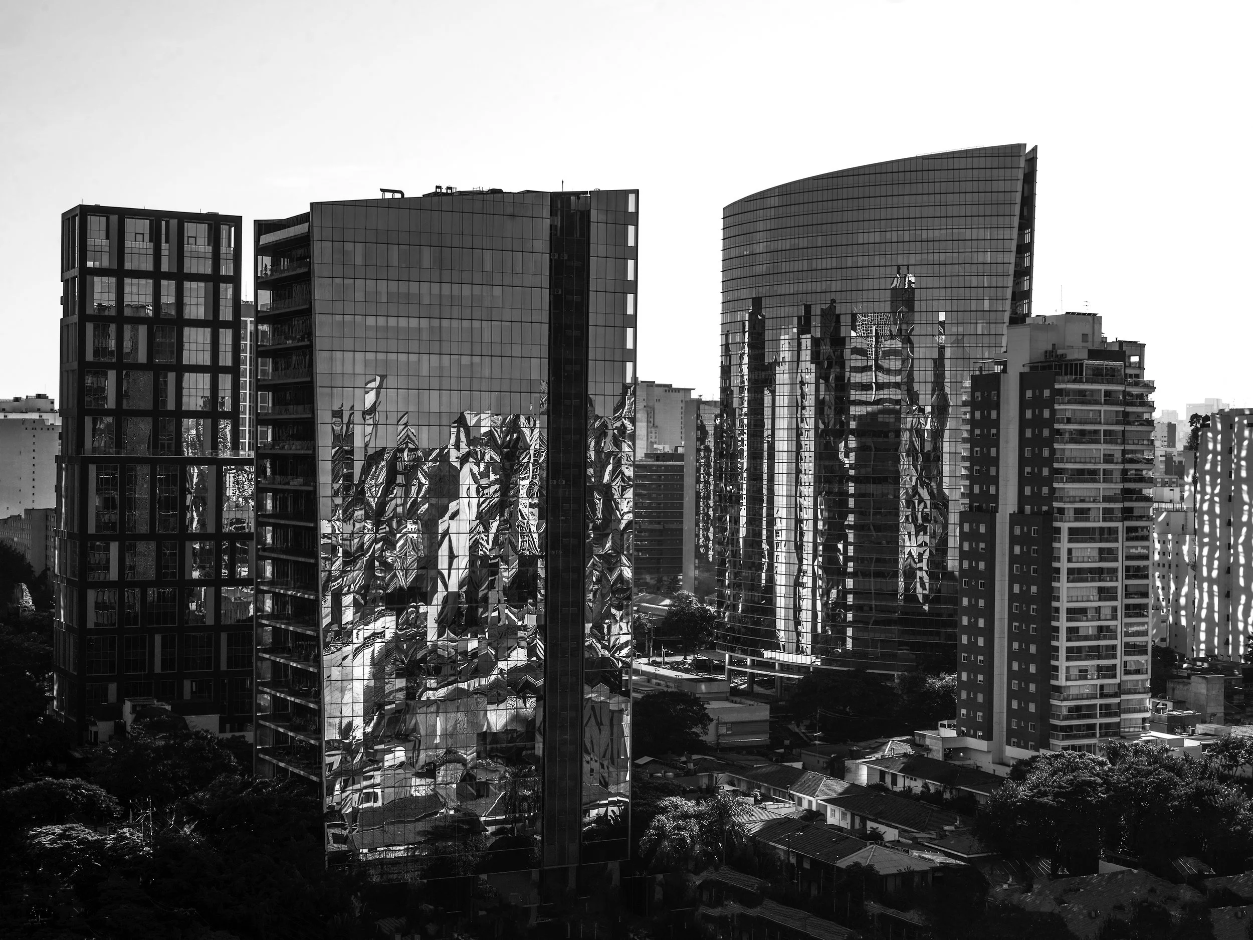 Foto de prédios altos de fachada de vidro refletindo outros edifícios, em uma paisagem urbana, em preto e branco.