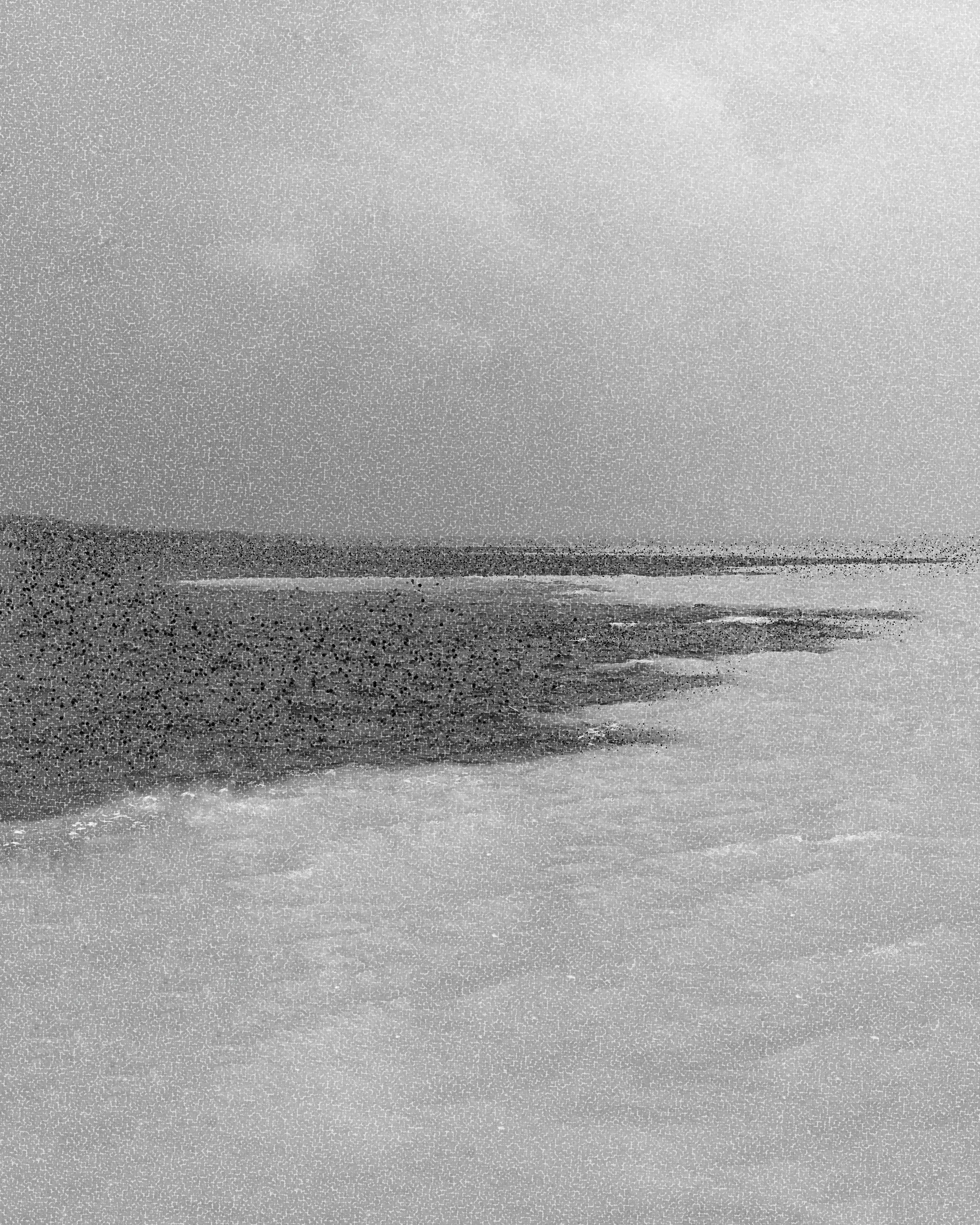 Praia de areia com mar agitado ao fundo, vista de um lado da praia.