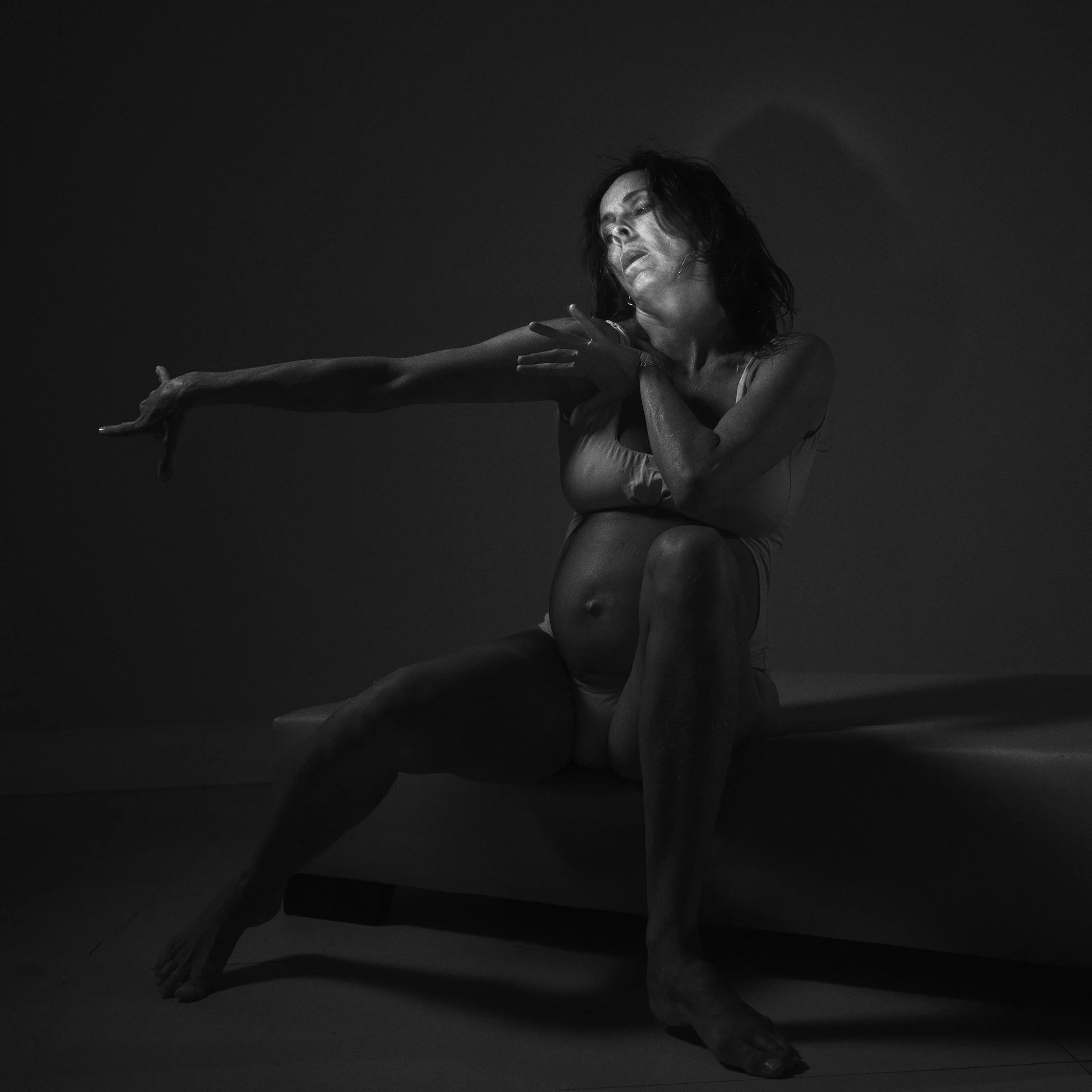 Mulher posando em um cenário escuro, com iluminação focada, criando um efeito dramático na fotografia em preto e branco.