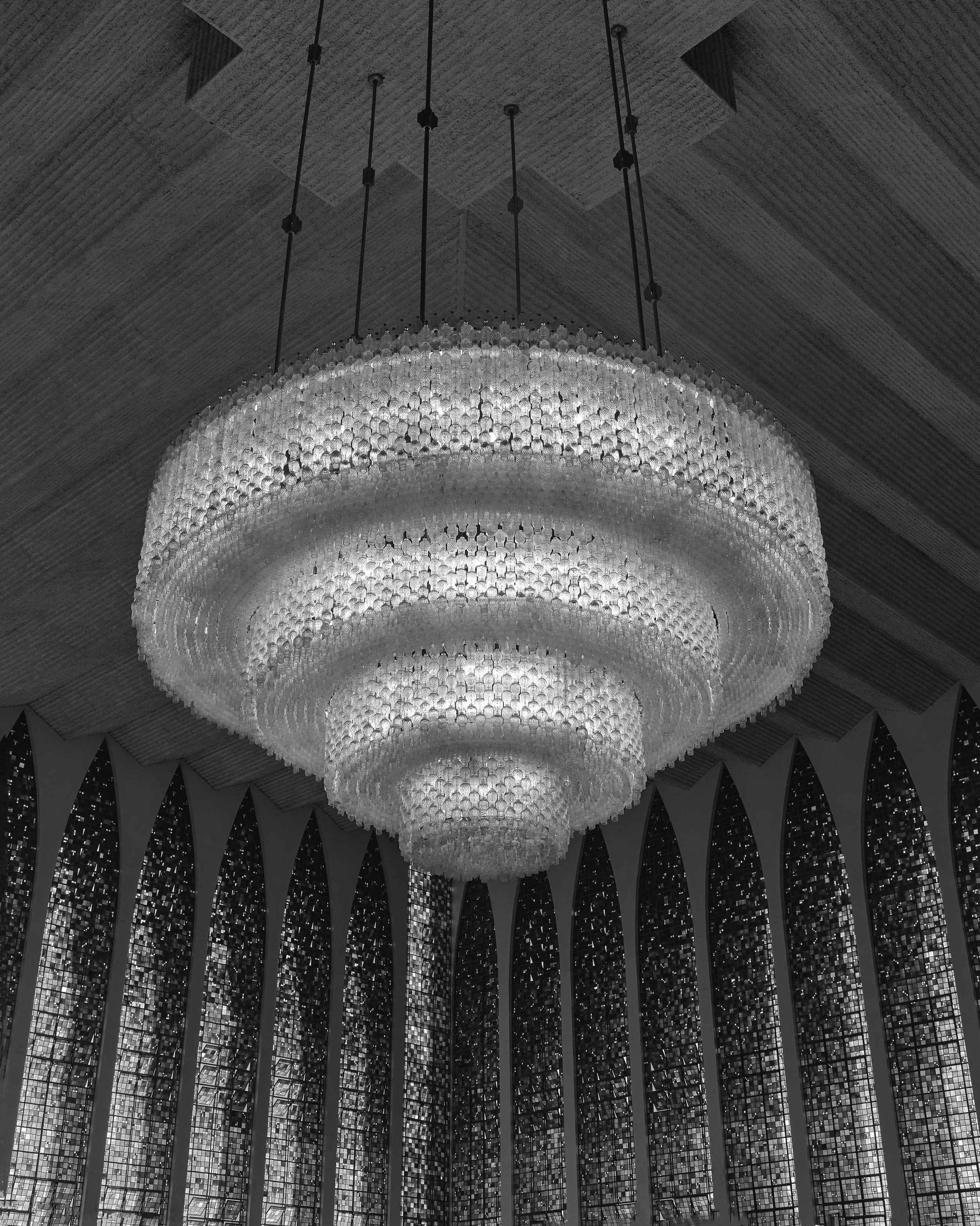 Cachorro de pelúcia gigante pendurado no teto de uma igreja, decorada com vitrais e uma luz dourada ao fundo.