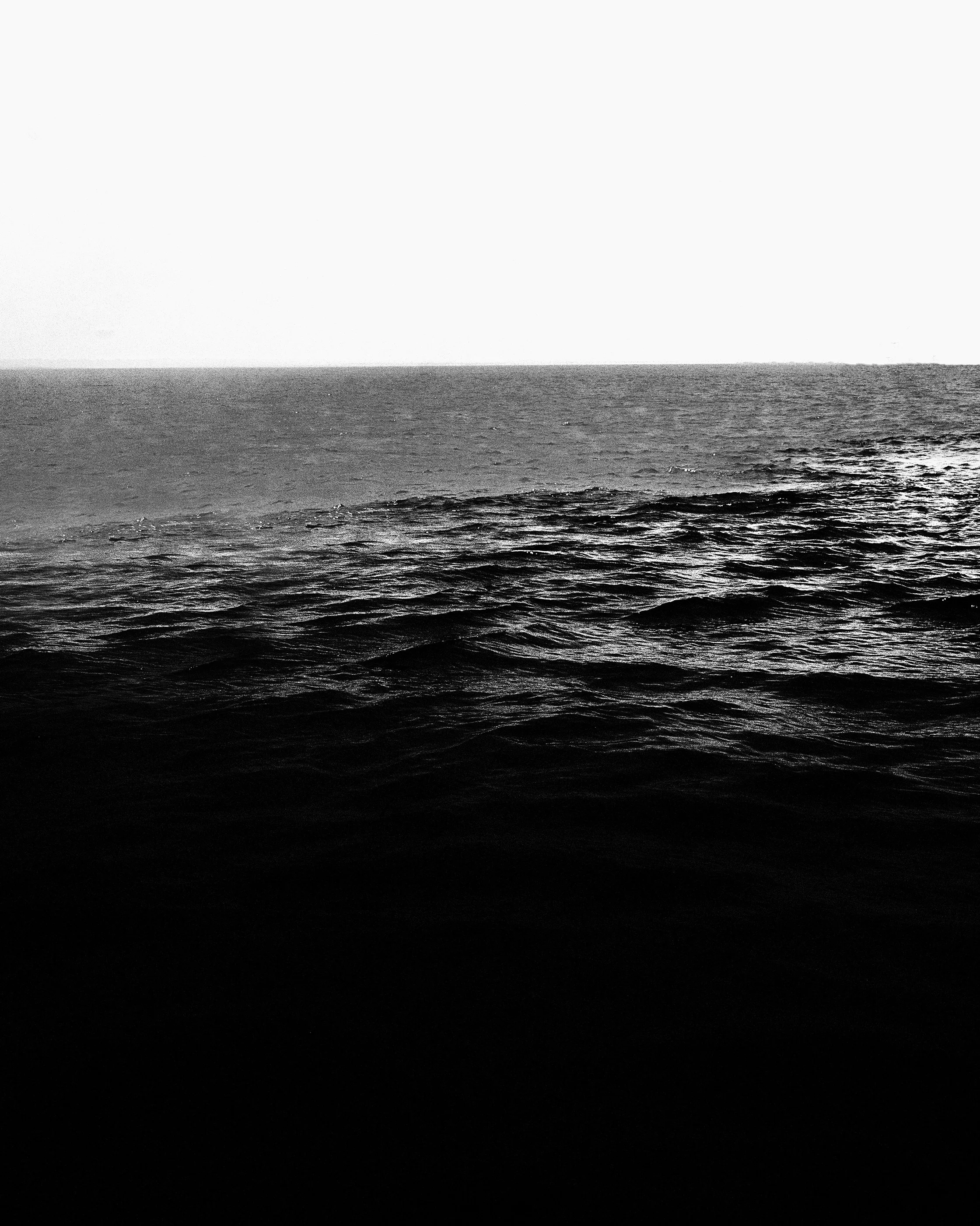 Imagem em preto e branco de um mar calmo com ondas suaves, sob um céu claro.