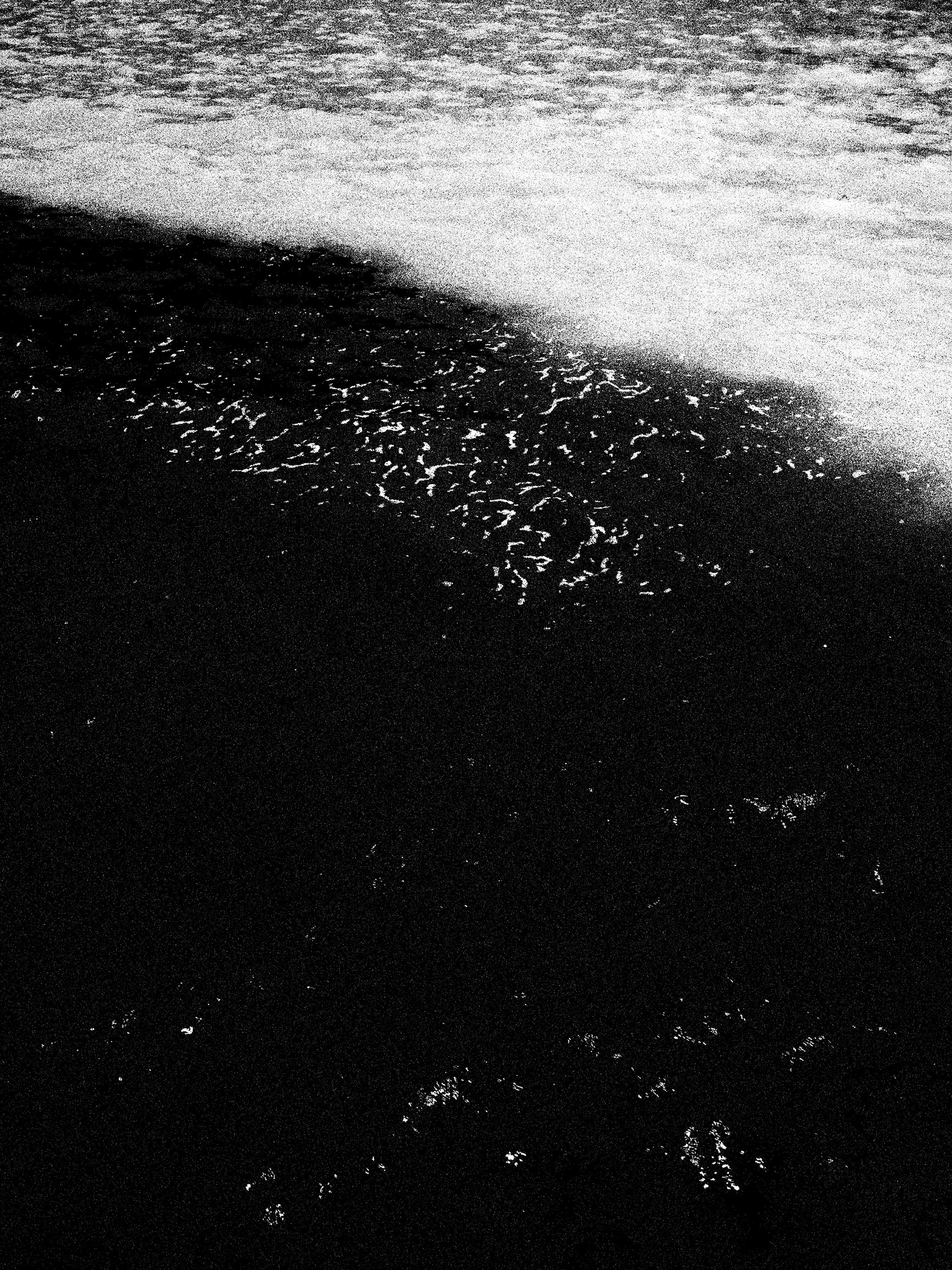 Ondas do mar se aproximando na praia, vista em preto e branco.