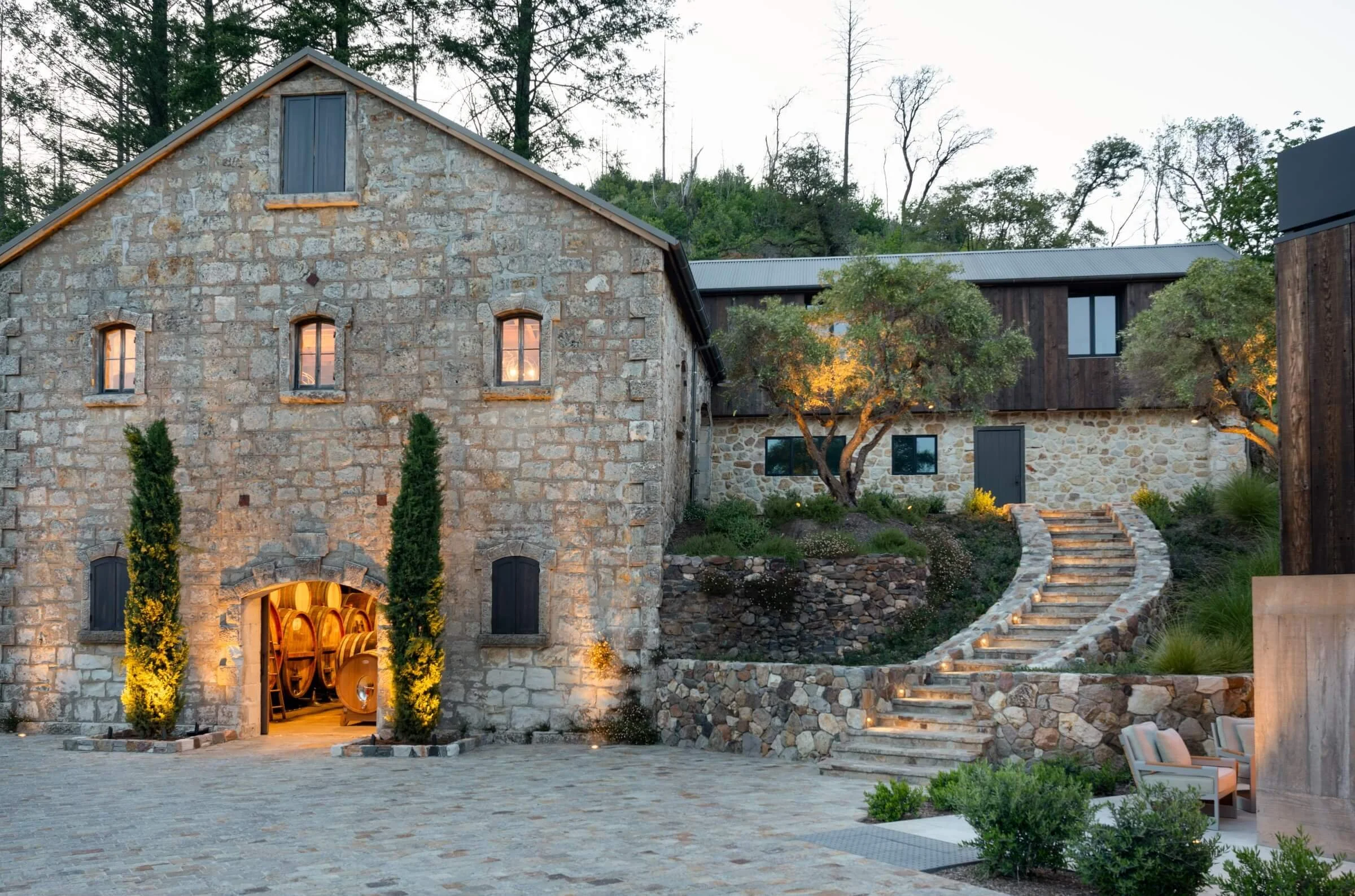 Exterior view of the Mayacamas Vineyards hospitality center in Napa Valley, showcasing custom architectural lighting for outdoor terraces and a historic stone facade at dusk.