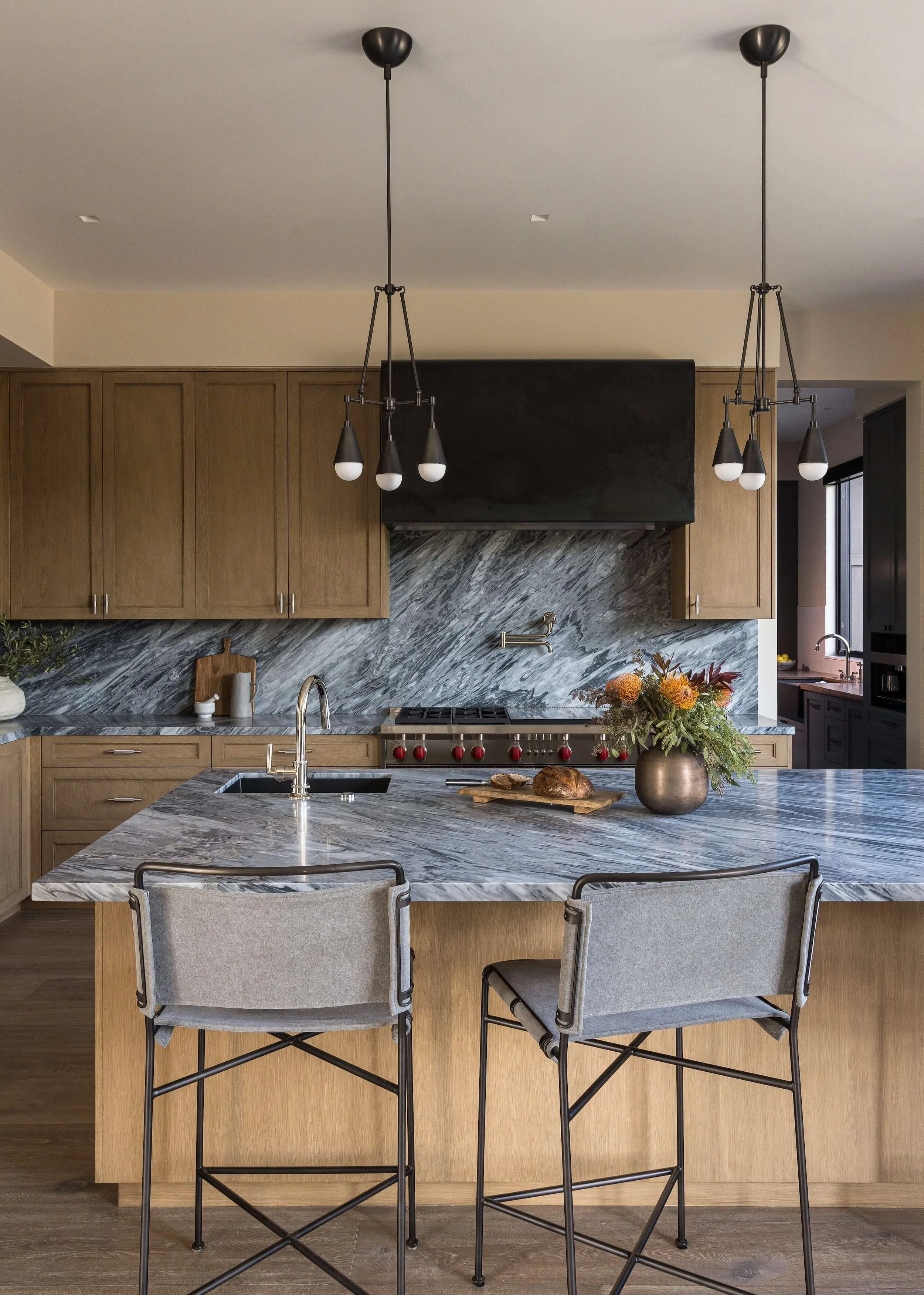 Sleek architectural pendant lighting over a marble waterfall island in a high-end custom kitchen.