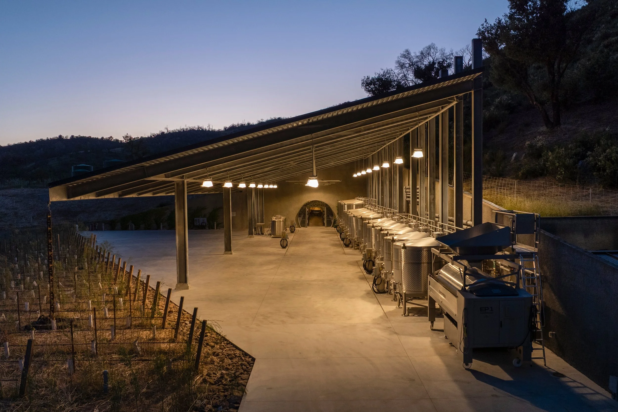 Layered exterior lighting extends the winery experience outdoors, highlighting the covered terrace and surrounding vineyard at dusk.