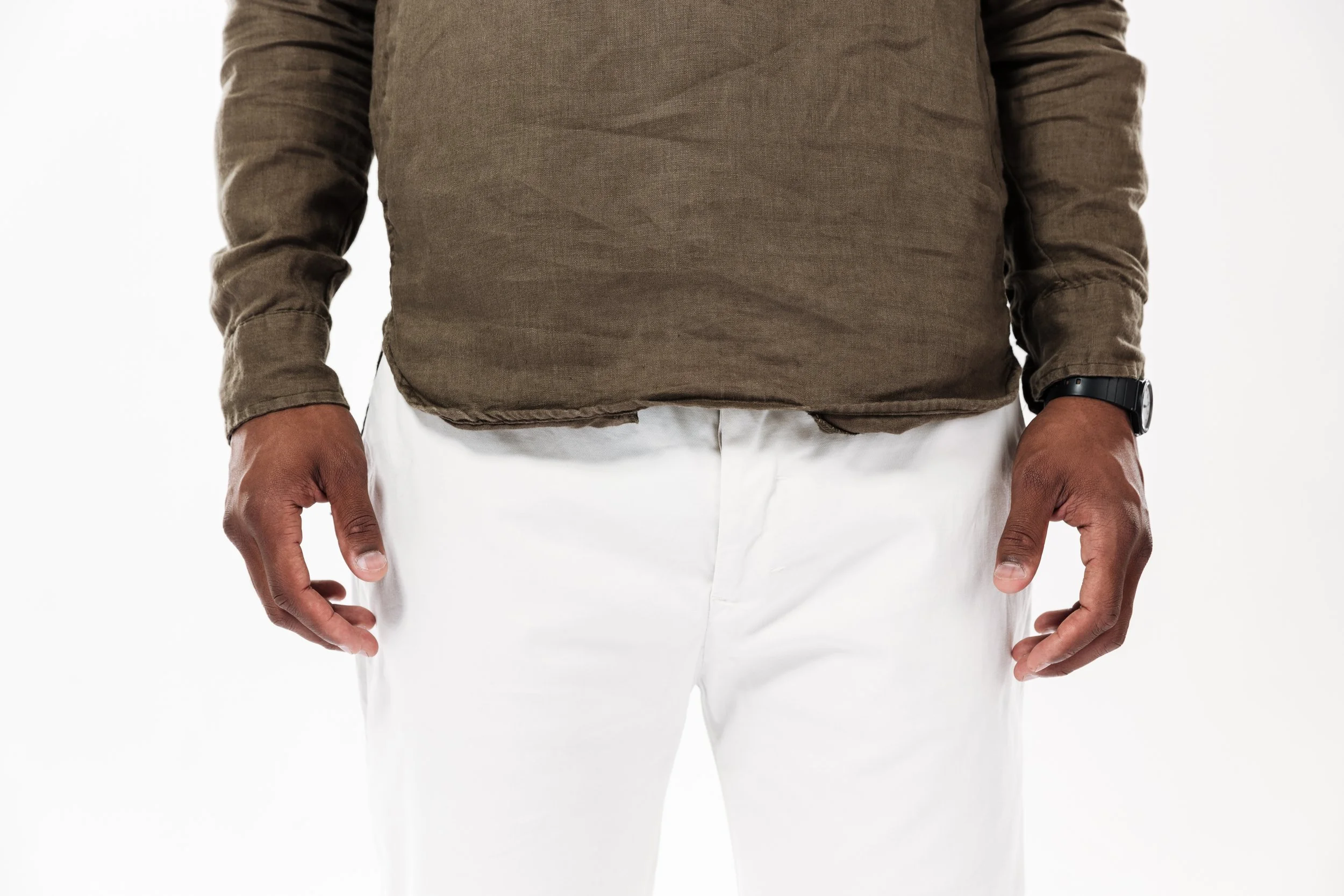 Close-up of a person wearing a green long-sleeve shirt, white pants, and a black watch, standing with arms relaxed at the sides.