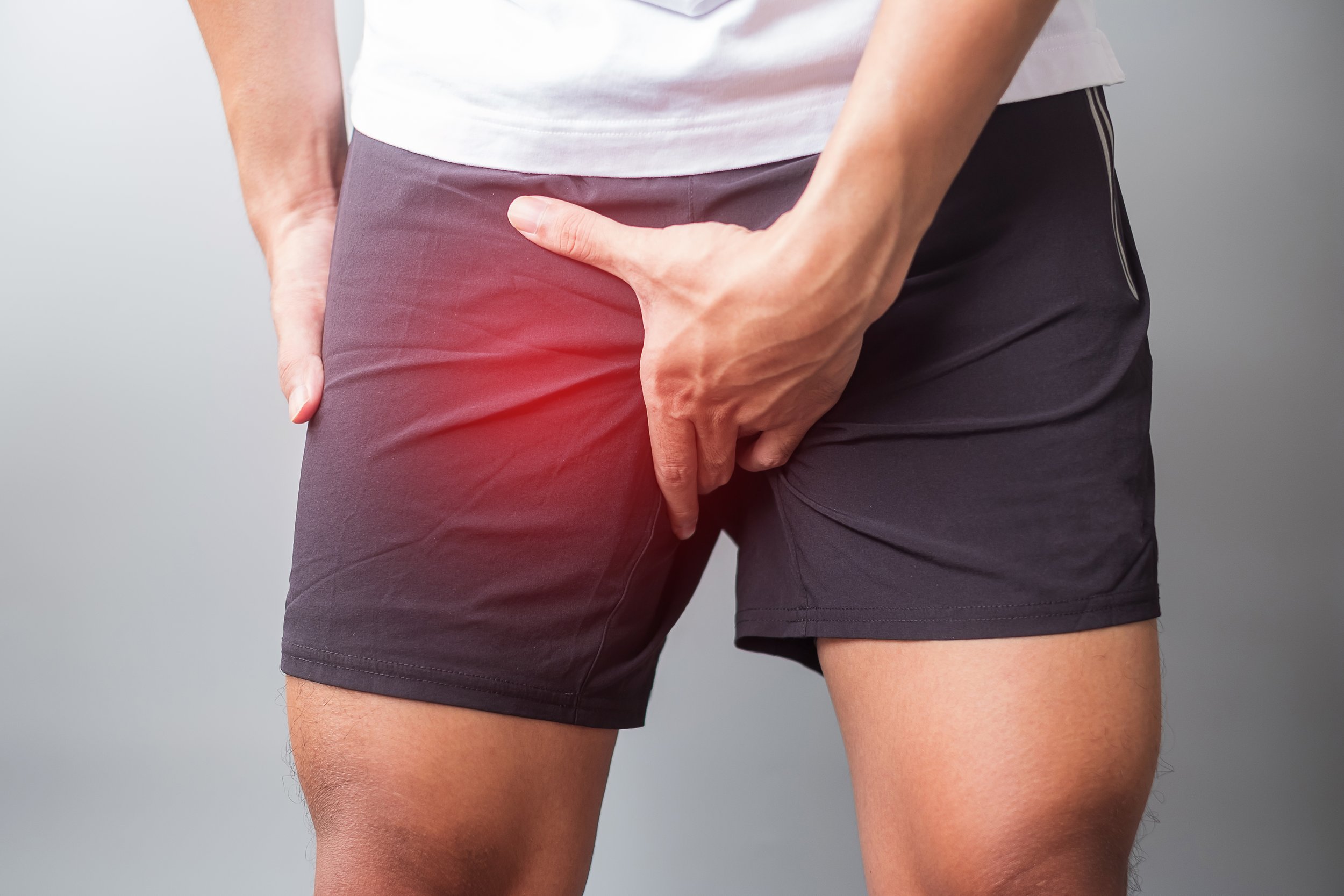 Person wearing black athletic shorts with a hand covering the groin area, with a red highlight around the area indicating discomfort or pain.
