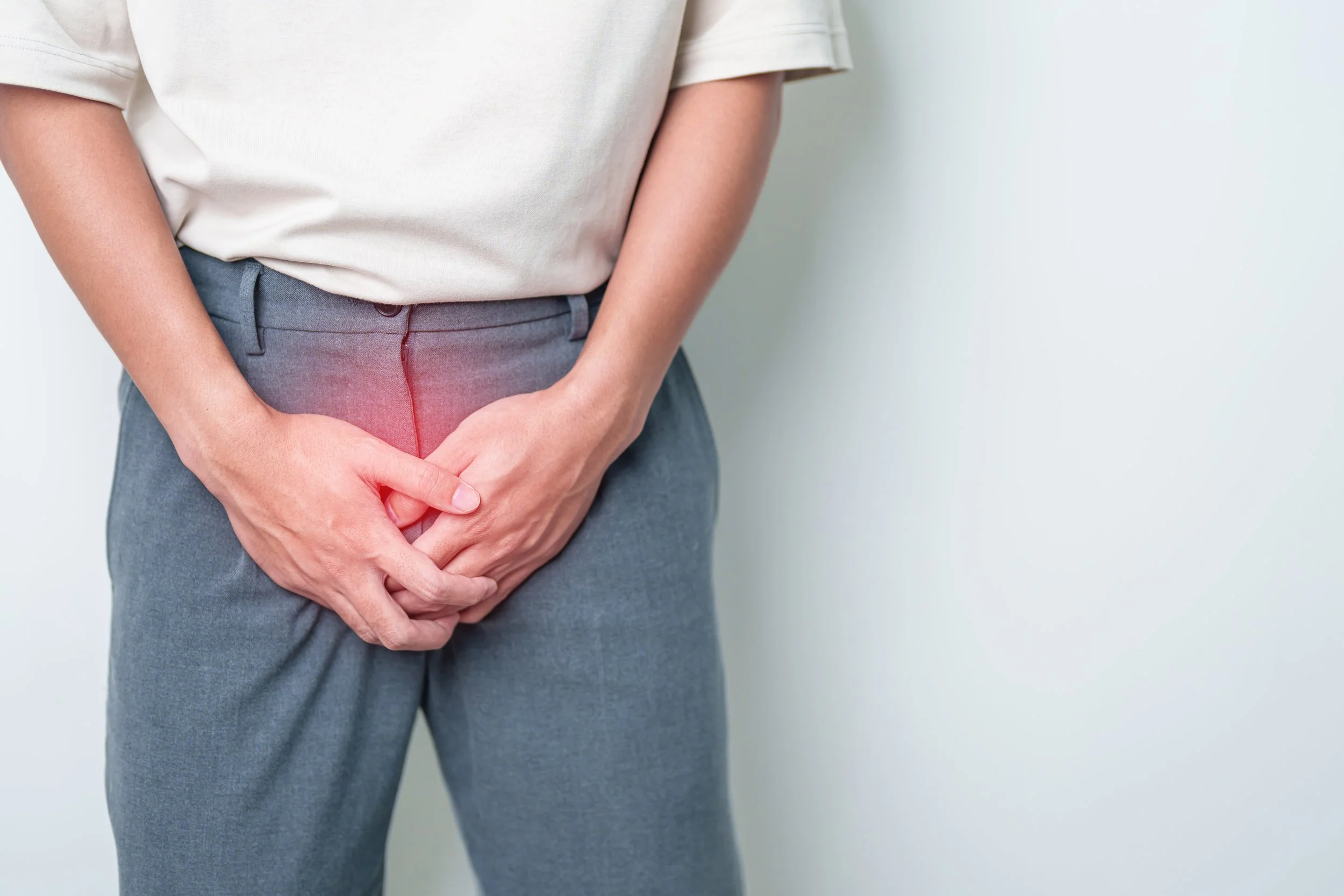 Person wearing a white shirt and gray pants holding their lower abdomen, indicating possible stomach pain.
