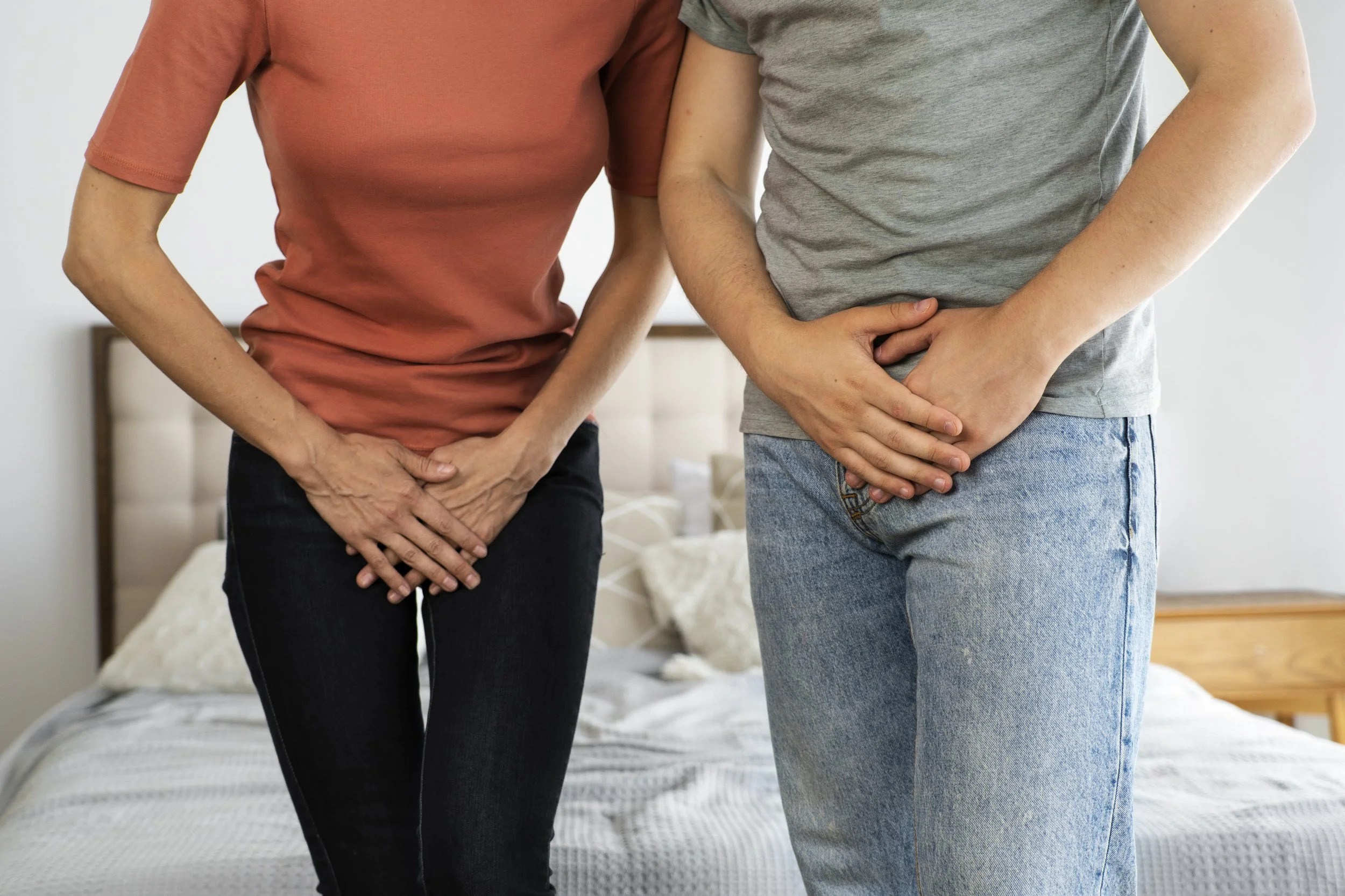 Two people standing on a bed with their hands over their lower abdomen.