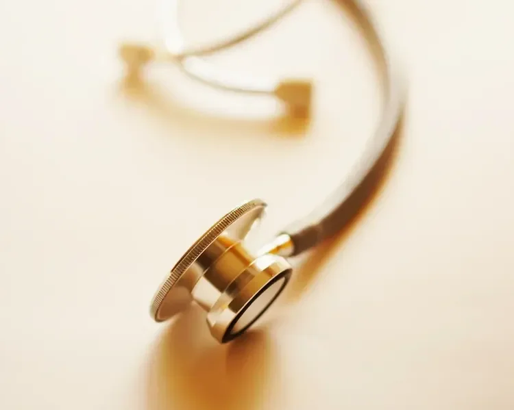 Close-up of a stethoscope with a gold chest piece and black tubing, lying on a light-colored surface.