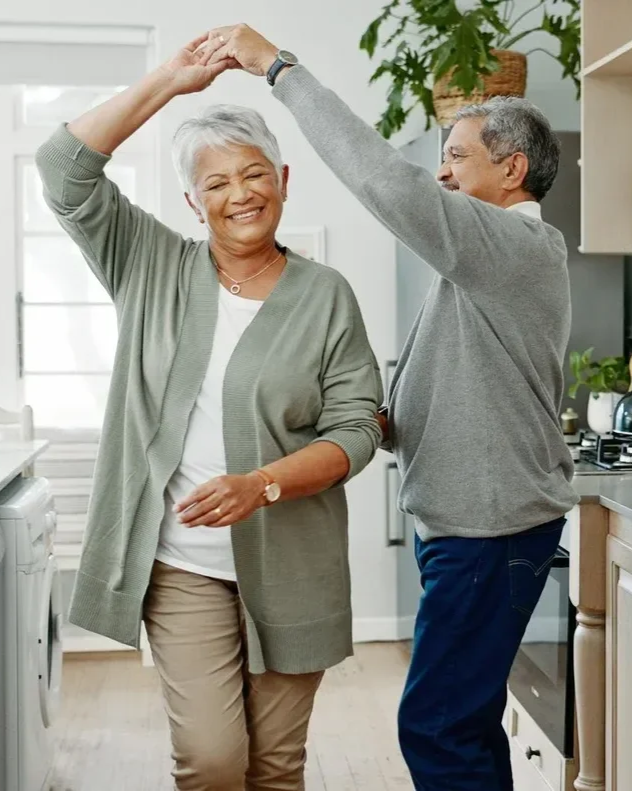 An elderly couple dancing together happily in their kitchen.