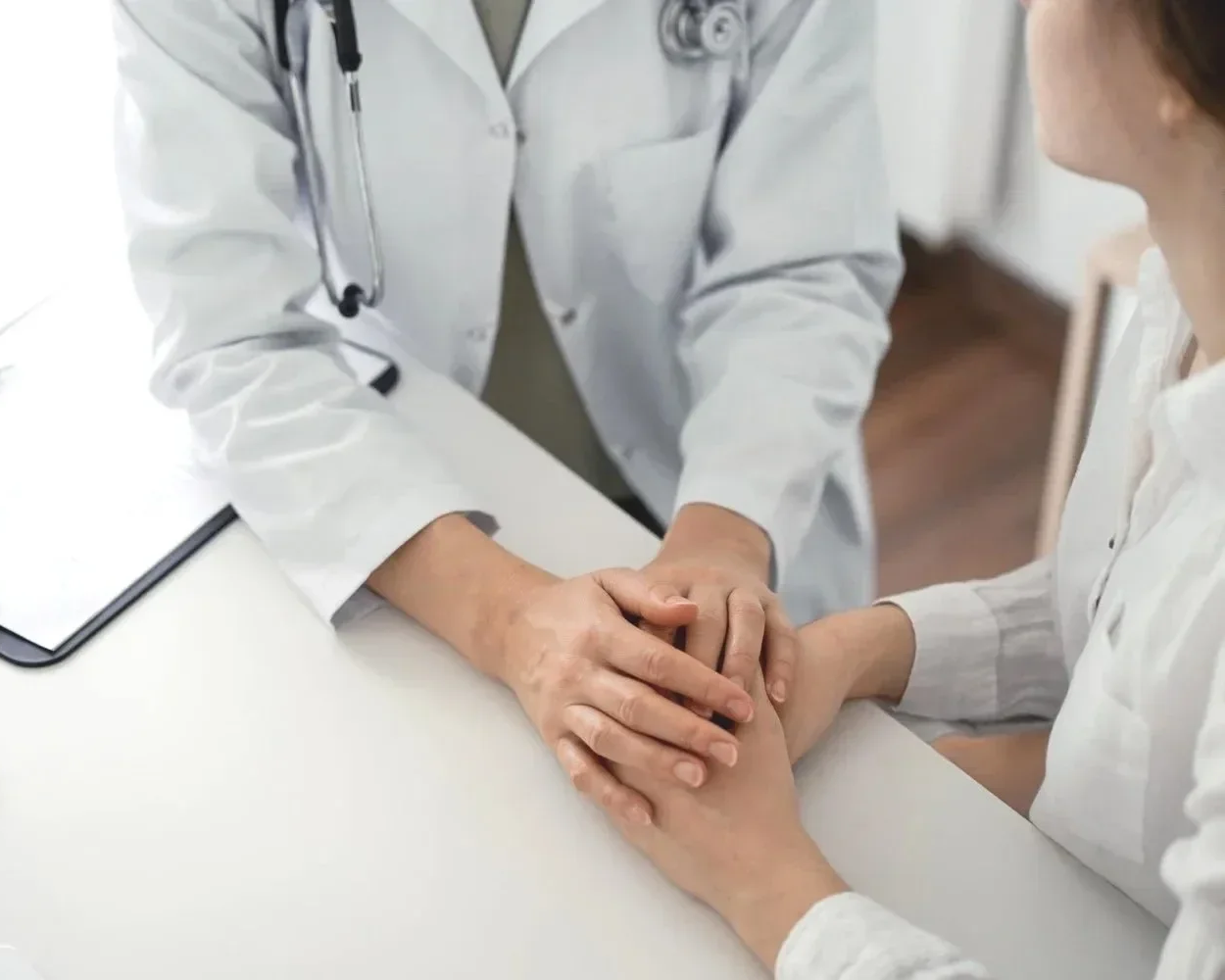 A healthcare professional holding a patient's hand in a comforting manner during a medical consultation.