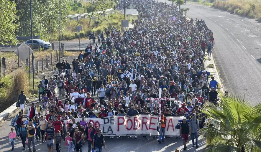 Large group of people protesting or marching on a highway, holding banners with Spanish text, some carrying umbrellas.
