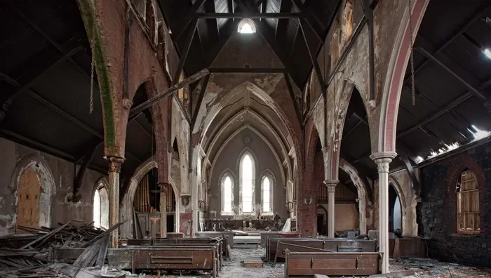 Inside an abandoned, dilapidated church with broken pews, damaged walls, and a partially collapsed ceiling, with sunlight streaming through the remaining stained glass windows.