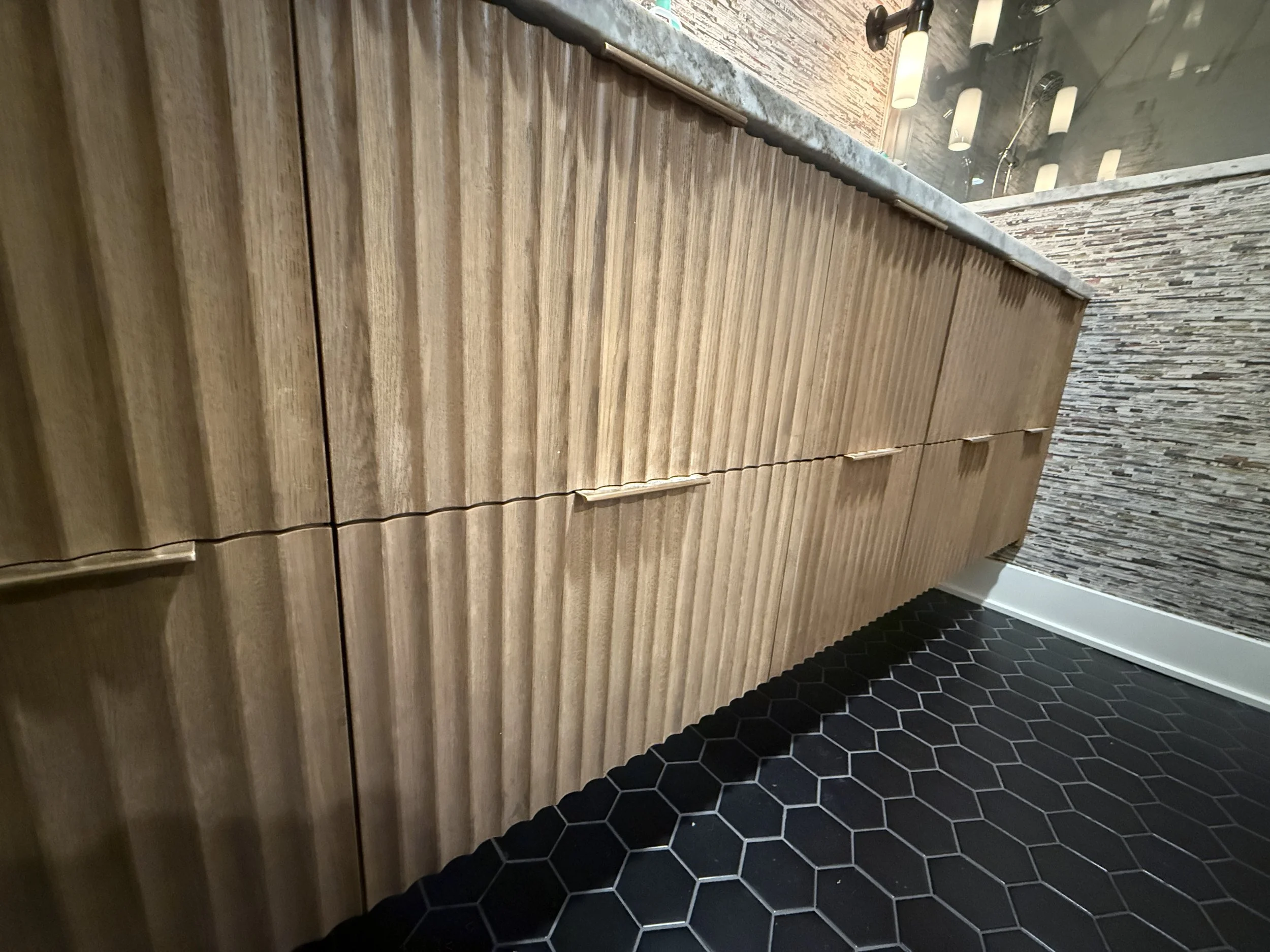 Wooden counter with a stone countertop in a modern interior space, black hexagon floor tiles, and a wall with a textured brick pattern.