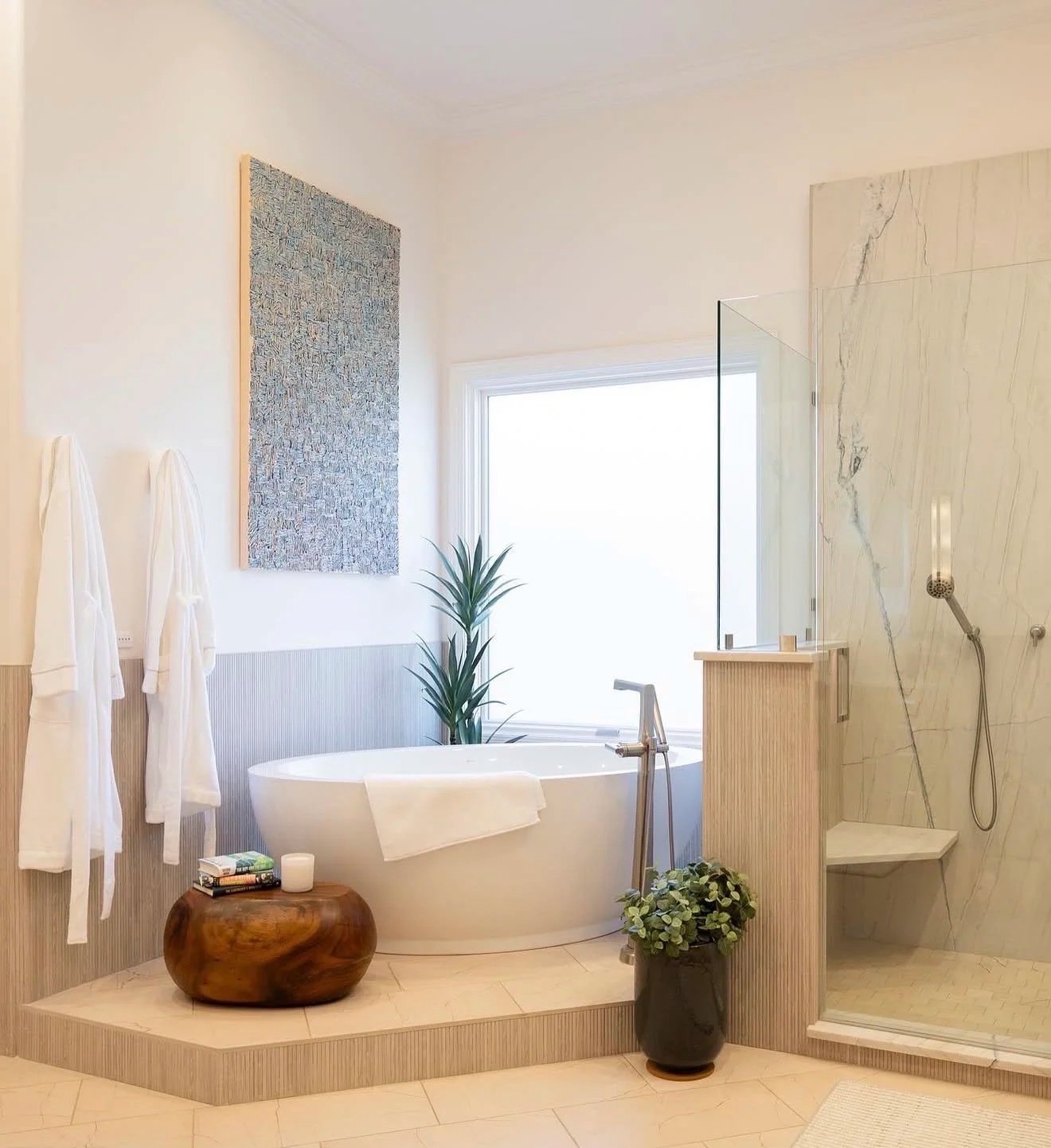 Modern bathroom with a bathtub, shower area, and decorative plants, featuring neutral tones and natural textures.