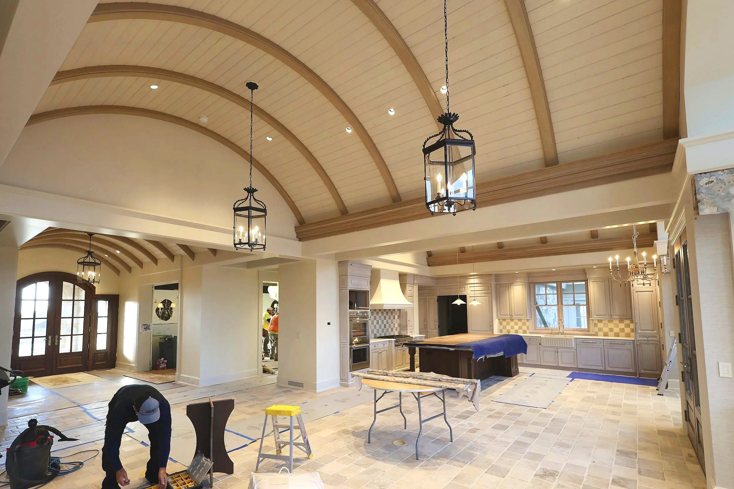 Interior view of a large kitchen under construction, featuring a vaulted wooden ceiling with pendant lights, an island, and cabinetry in progress.