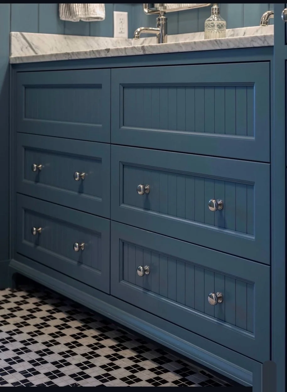 Blue bathroom vanity with six drawers and a marble countertop, featuring silver knobs, against a tiled wall and a black and white checkered floor.