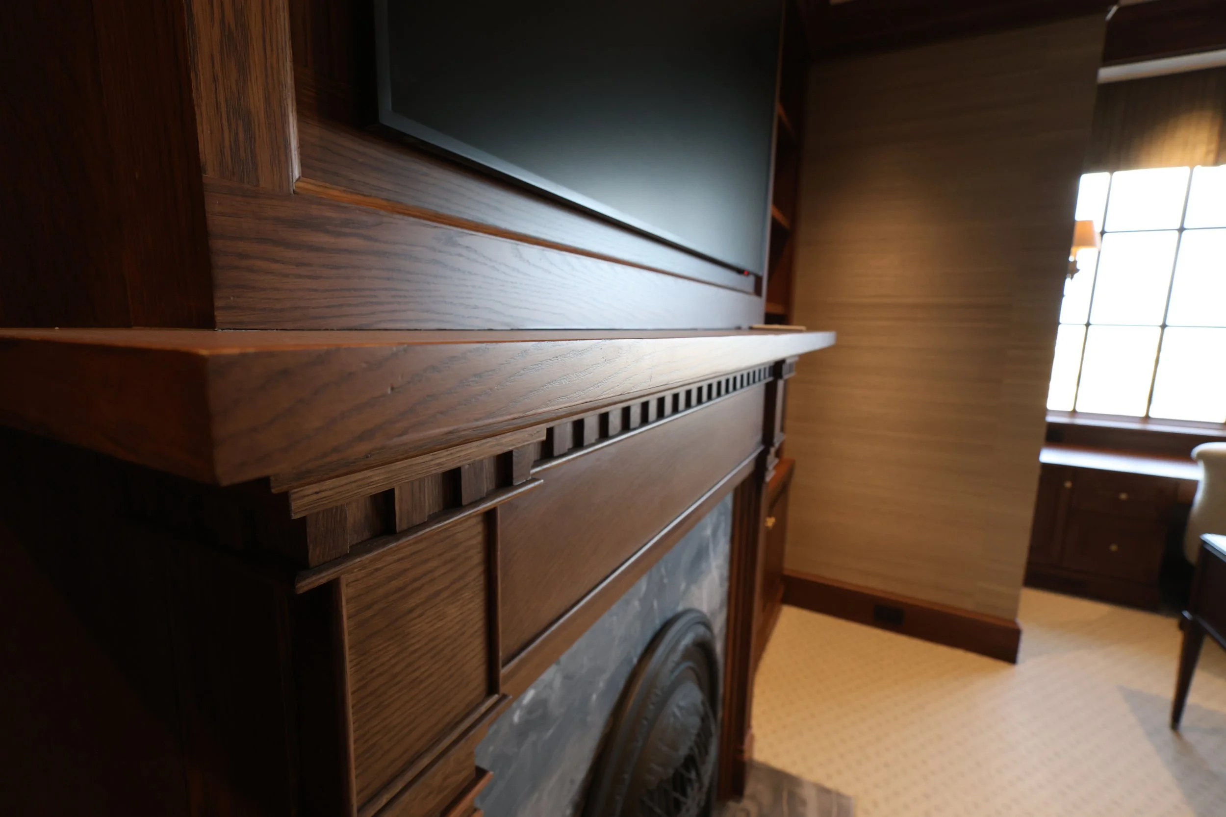 Interior of a room with dark wooden paneling, a large flat-screen TV on a wooden stand, and a window with multiple panes allowing natural light.