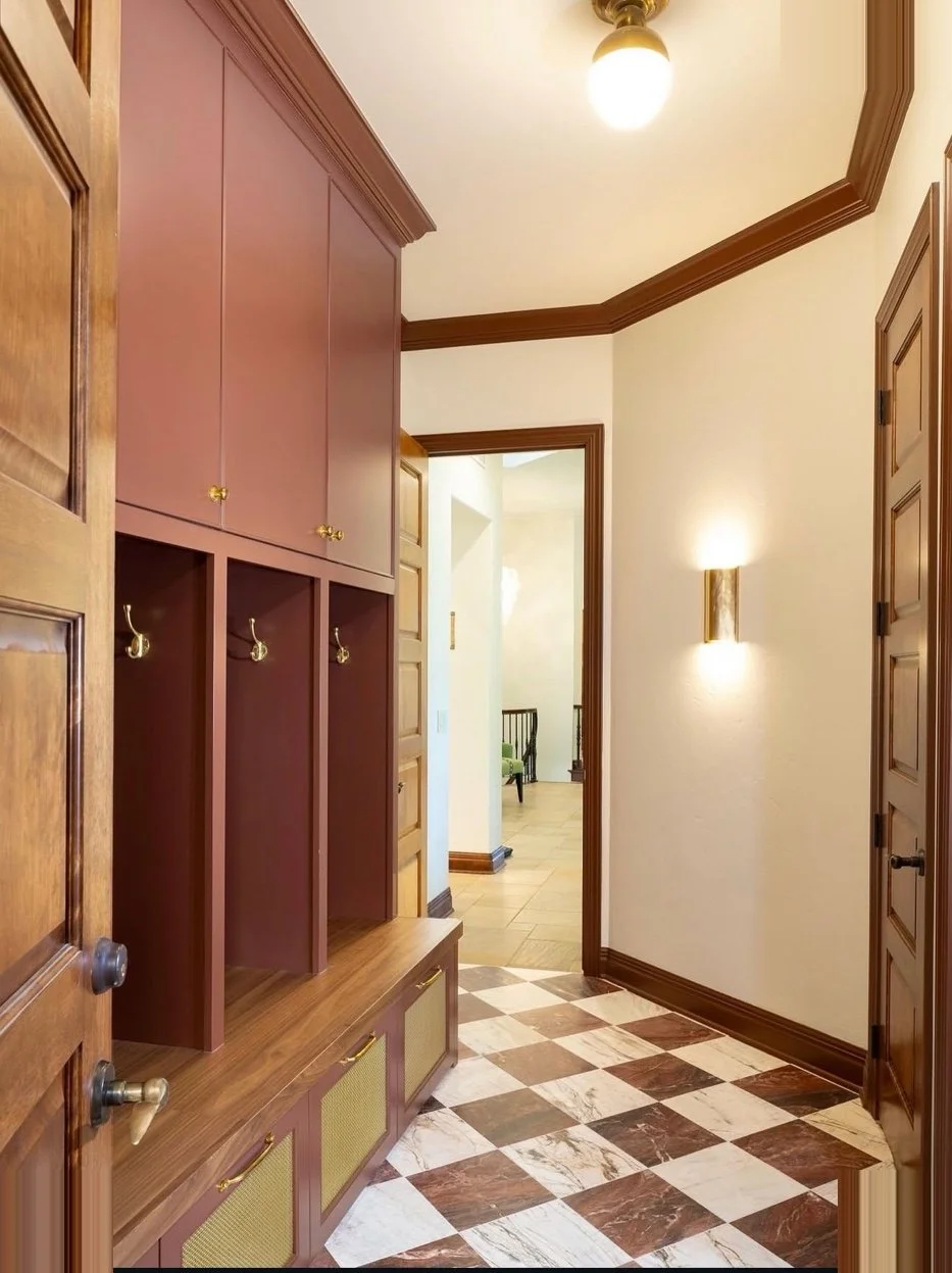 Interior entryway with wooden cabinets, checkered marble floor, wall light, and doorway leading to a brighter room.