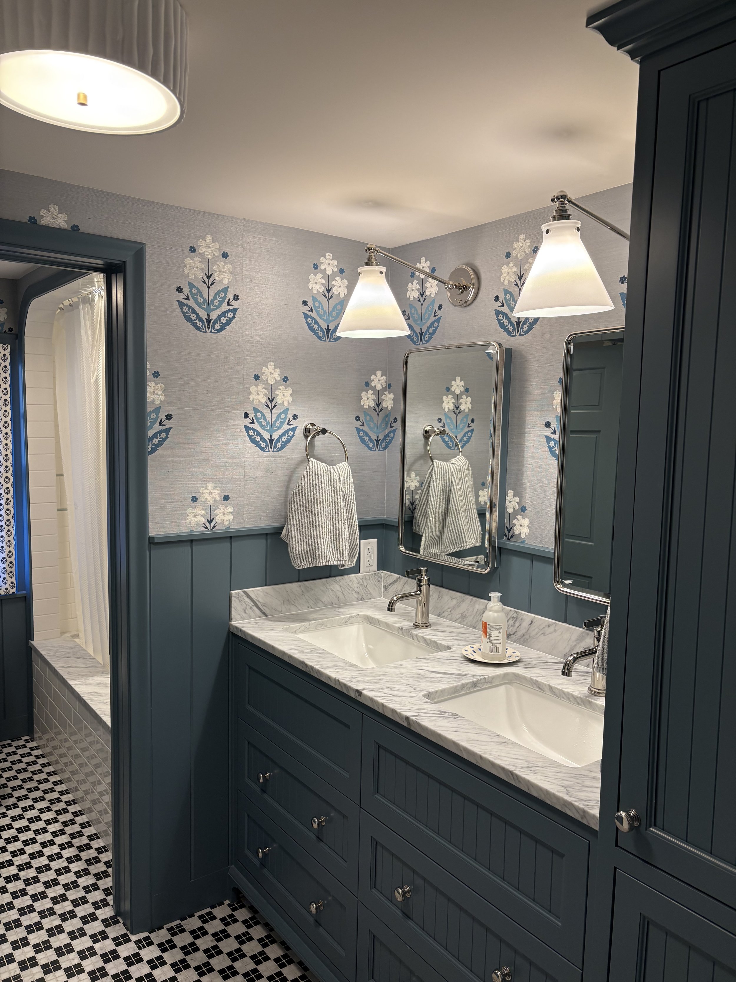 Bathroom with dark blue cabinetry, marble countertop, rectangular undermount sink, wall-mounted mirrors, wall-mounted lights, towel with stripes, and a mosaic tile floor.