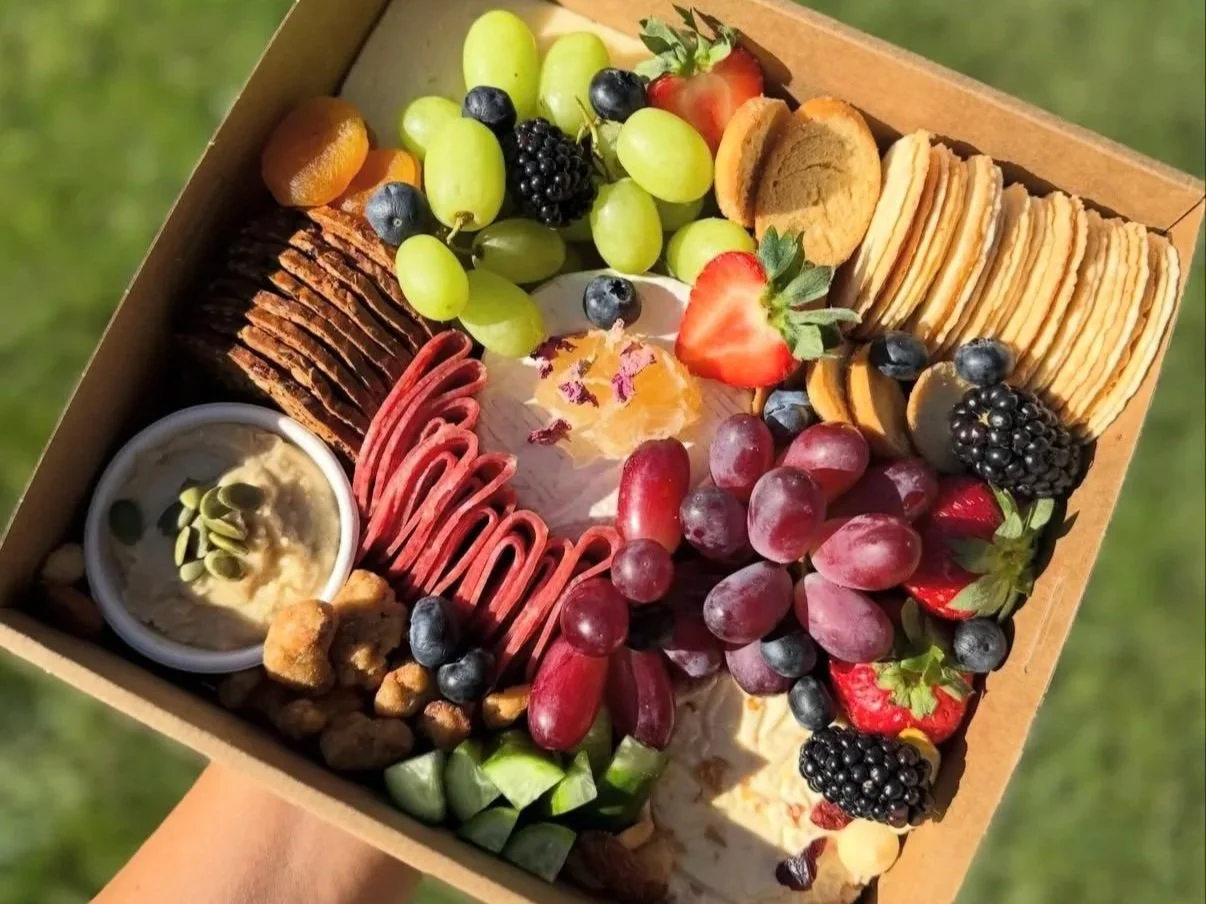 A box of assorted snacks including grapes, strawberries, blackberries, cookies, crackers, dip, and other finger foods.