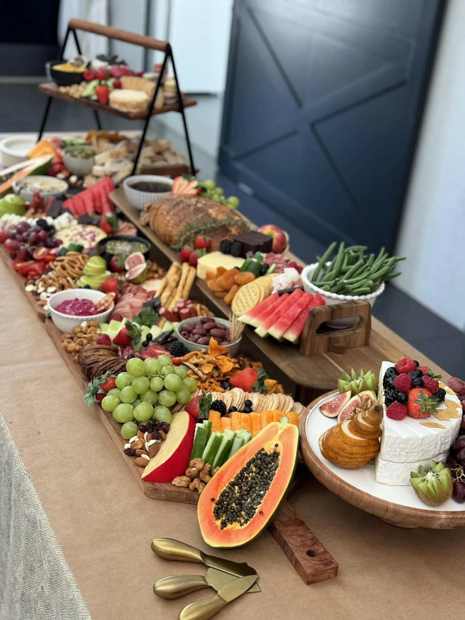 A large assortment of fruits, vegetables, cheeses, meats, and desserts arranged on a long wooden table for a buffet or celebration.