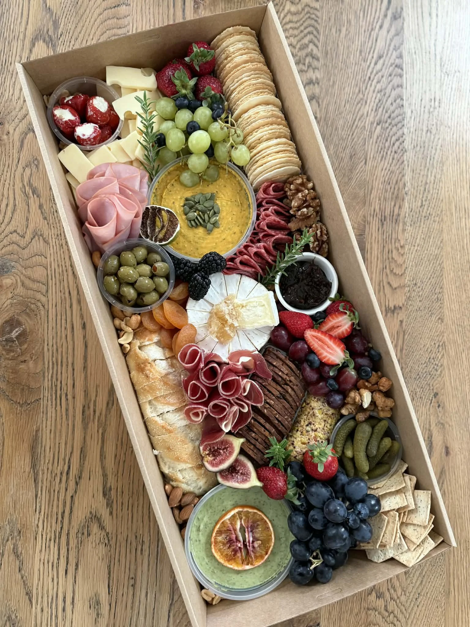 A large rectangular board of assorted cheeses, fruits, crackers, nuts, olives, cured meats, and dips arranged for a cheese platter.
