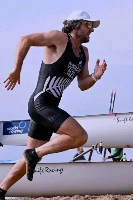 Man in athletic gear running on a beach with a rowing boat in the background.