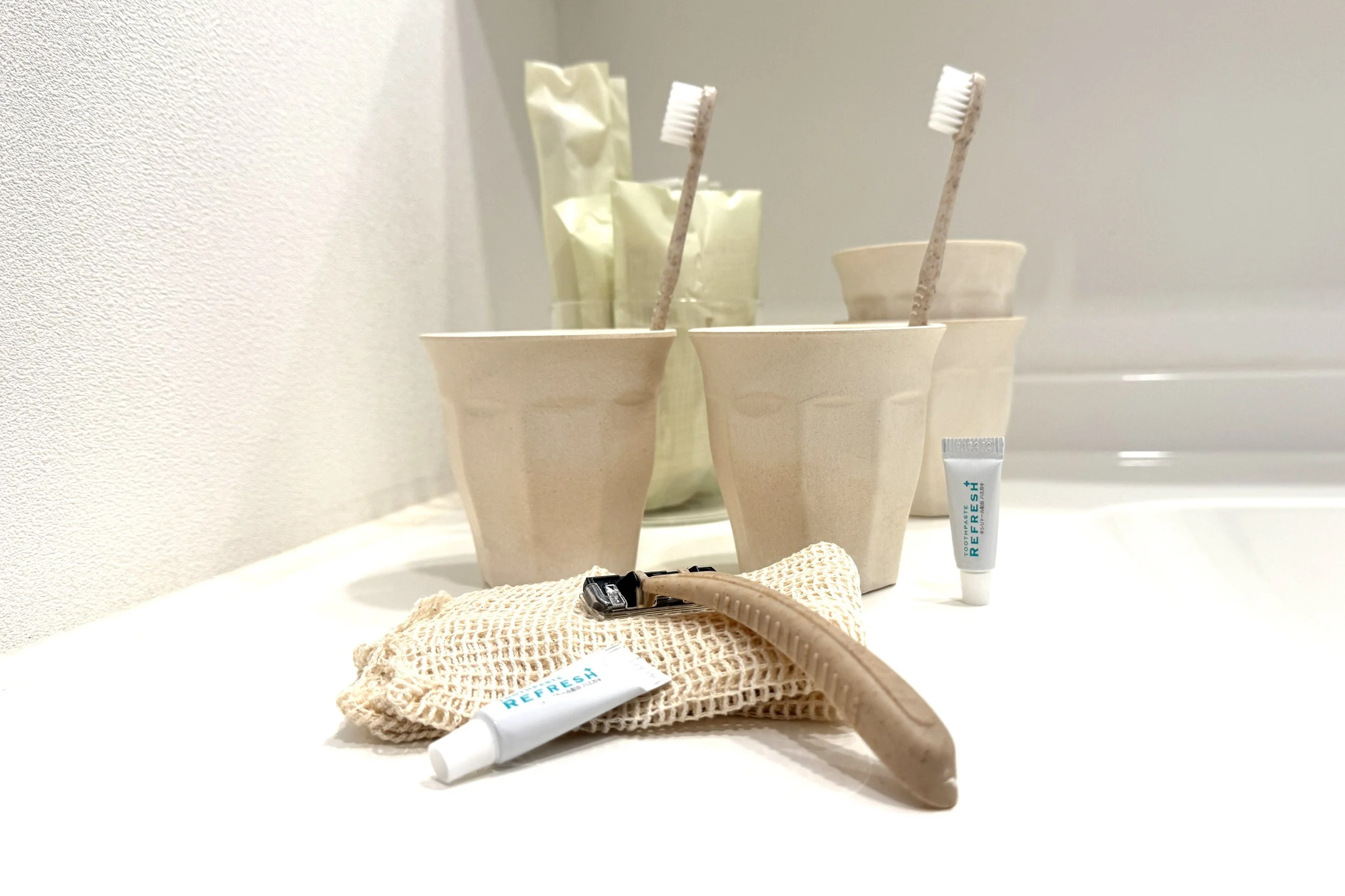 紙コップに歯ブラシと歯磨き粉のチューブ。背景にゴミ袋とその他の歯磨き用品。