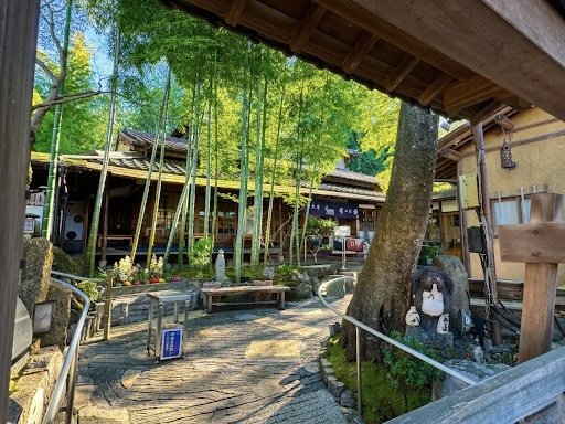 竹林と伝統的な日本建築の庭園風景。中に扉や木製の橋、蕎麦屋の看板やペンギンの置物が見える。
