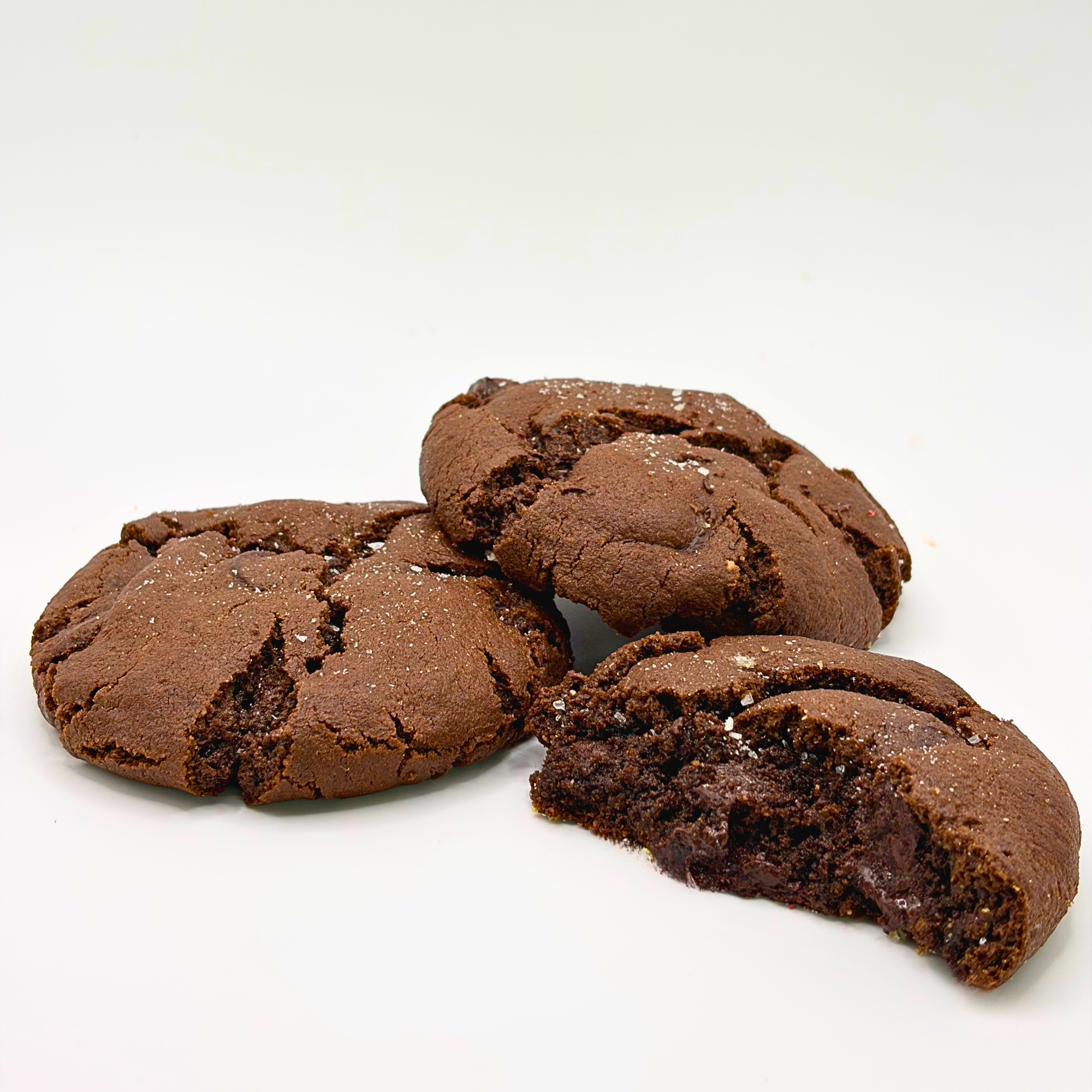 Chocolate cookies stacked on a white surface with one broken cookie revealing a gooey chocolate center.