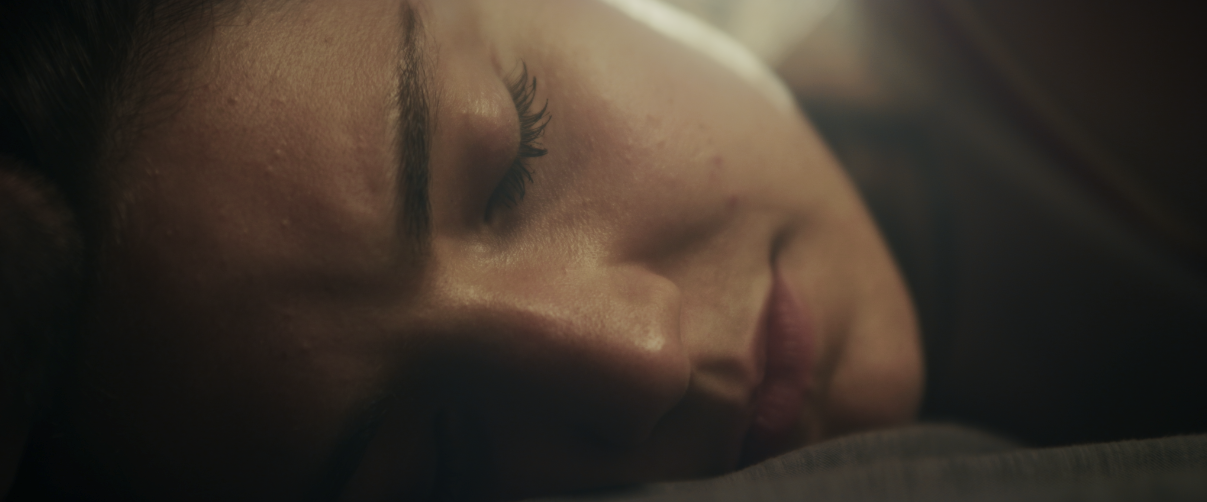 Close-up of a woman sleeping with her face resting on a surface, eyes closed, with soft lighting.