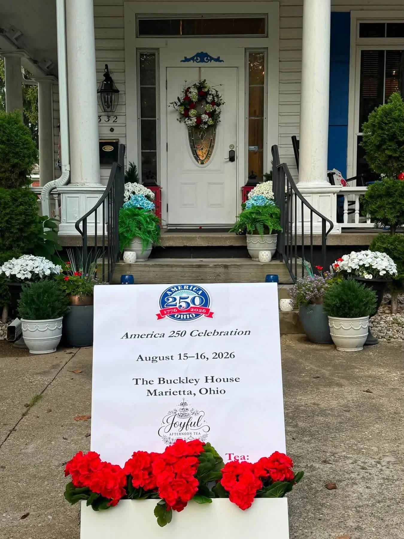 Front porch decorated with flowers and a sign celebrating America's 250th birthday, dated August 15-16, 2026, at The Buckley House in Marietta, Ohio.